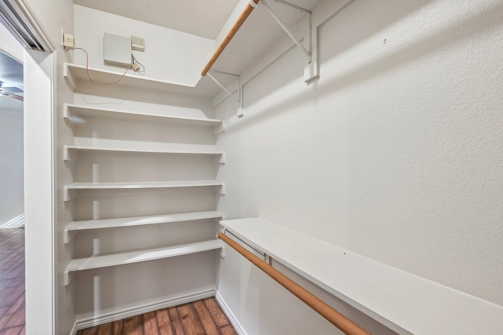 Built-in shelving, hanging rods, wood-finish flooring, and white painted walls
