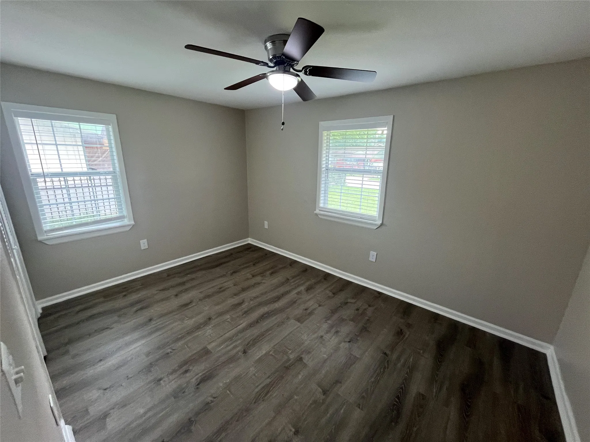 Room featuring neutral-toned walls, wood-finish flooring, two windows with horizontal blinds, and a central ceiling fan with an integrated light fixture