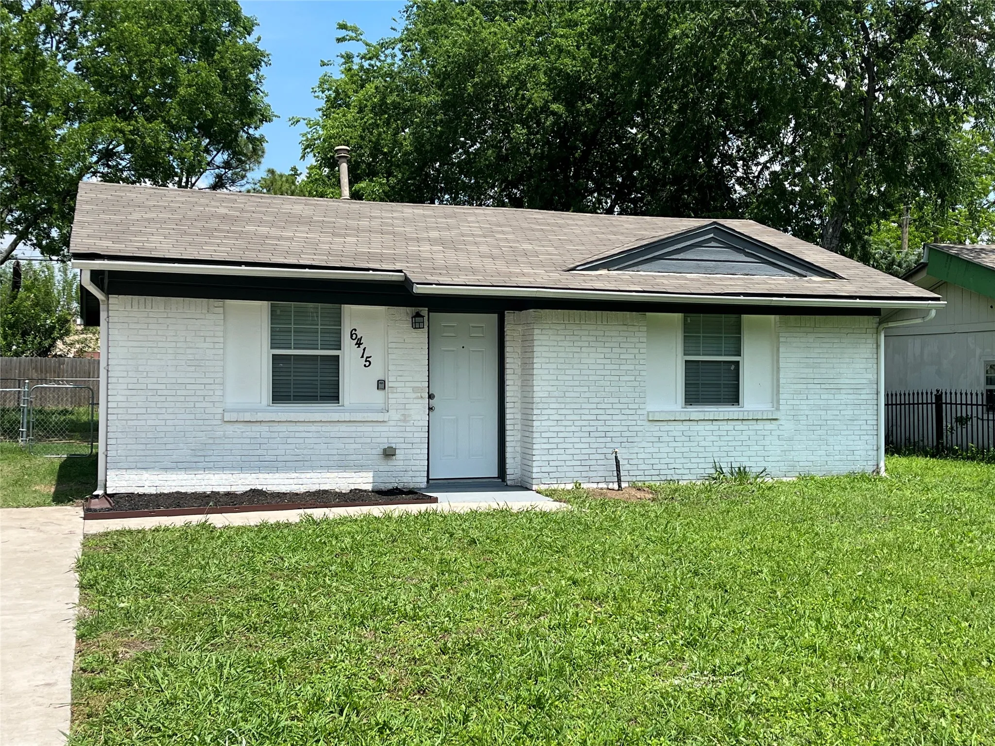 Single-story residence featuring white brick exterior, asphalt shingle gable roof, front-facing triangular gable vent, and concrete walkway