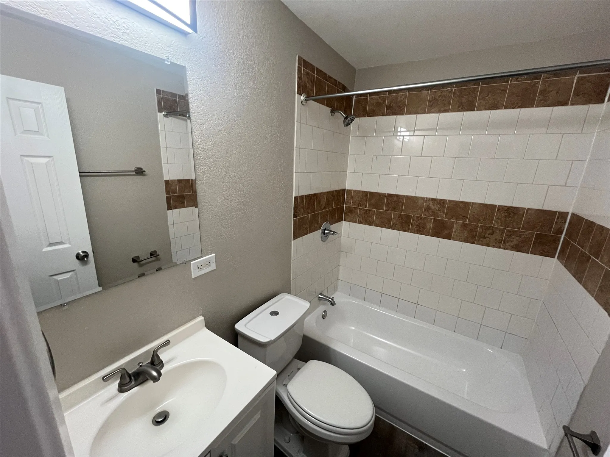 Bathroom featuring a white vanity with an integrated sink, polished chrome faucet, rectangular wall-mounted mirror, and a tub-shower combination with decorative tile inlay