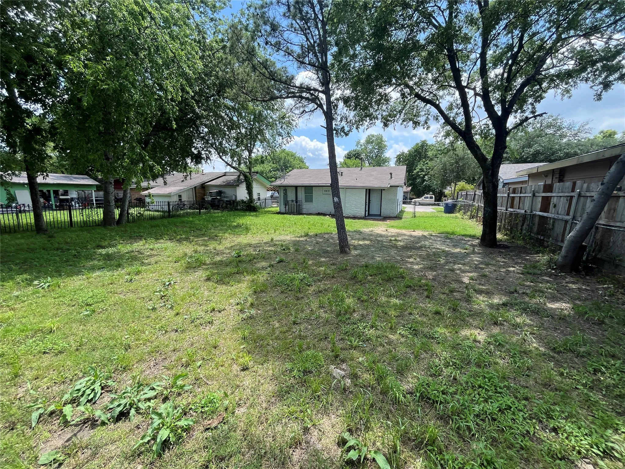 Expansive backyard featuring mature trees, wood fence perimeter, and metal rod fencing