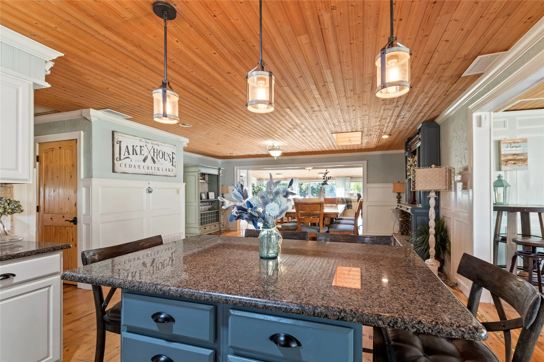 Kitchen featuring a central island with stone countertop, wood-plank ceiling, three industrial-style pendant lights, and beadboard wall paneling