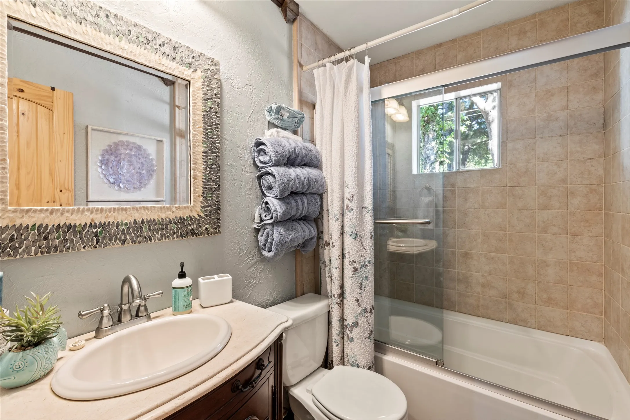 Bathroom featuring a vanity with a drop-in sink, a wall-mounted mirror with mosaic tile trim, and a bathtub-shower combination with a sliding glass door and tiled surround