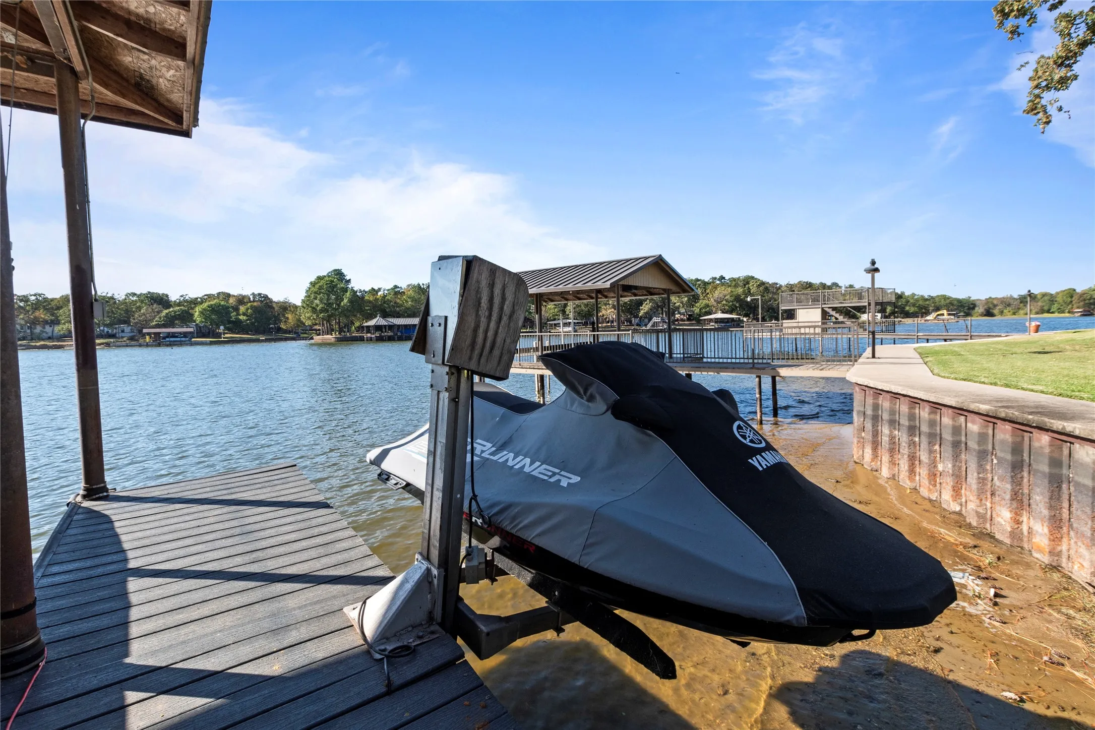 Private wooden dock featuring a mechanical personal watercraft lift, covered boat slip, steel bulkhead, and concrete shoreline path