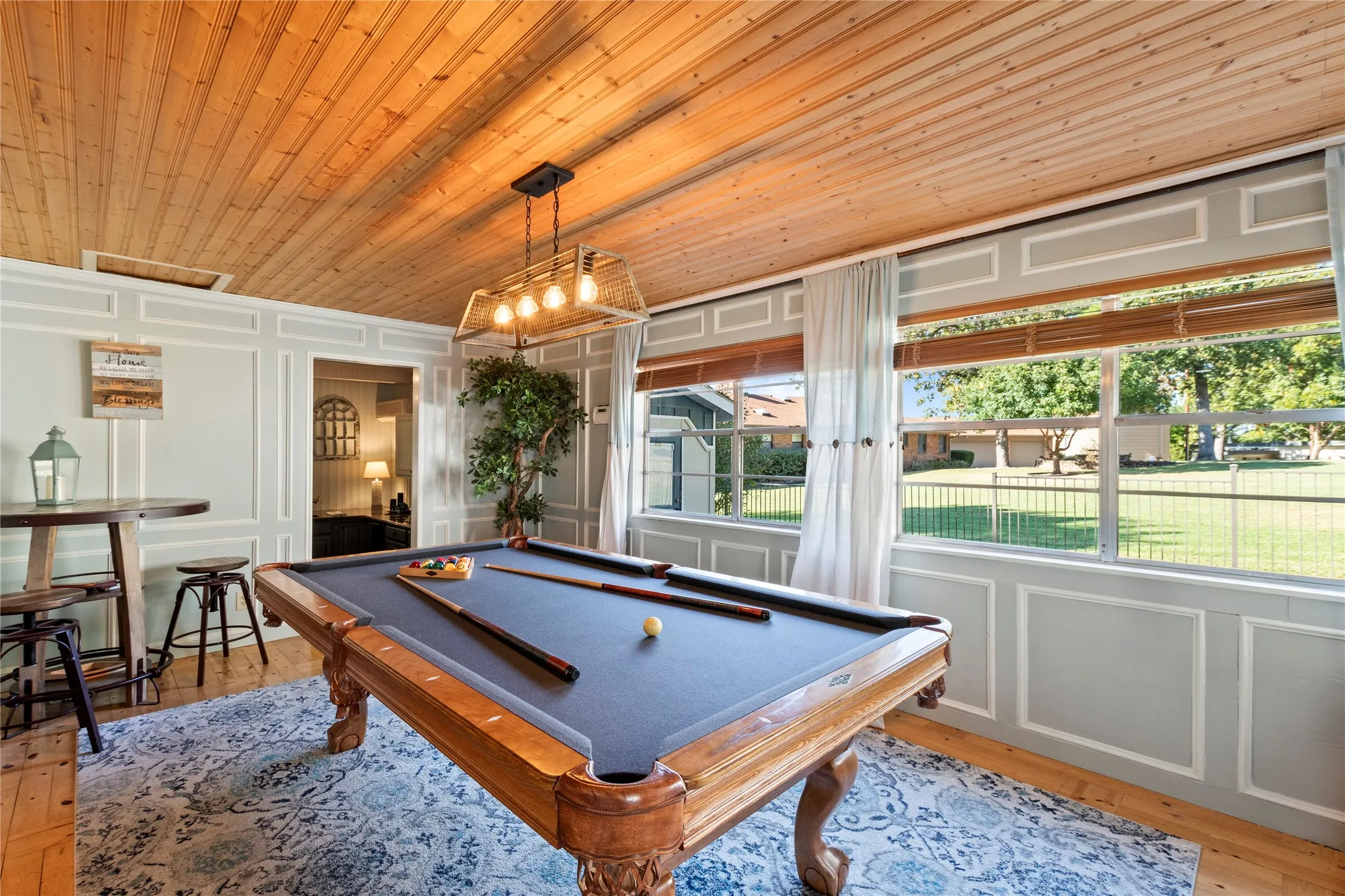 Beadboard wood-plank ceiling, wall wainscoting with decorative molding, large multi-pane windows, and a box-frame metal light fixture