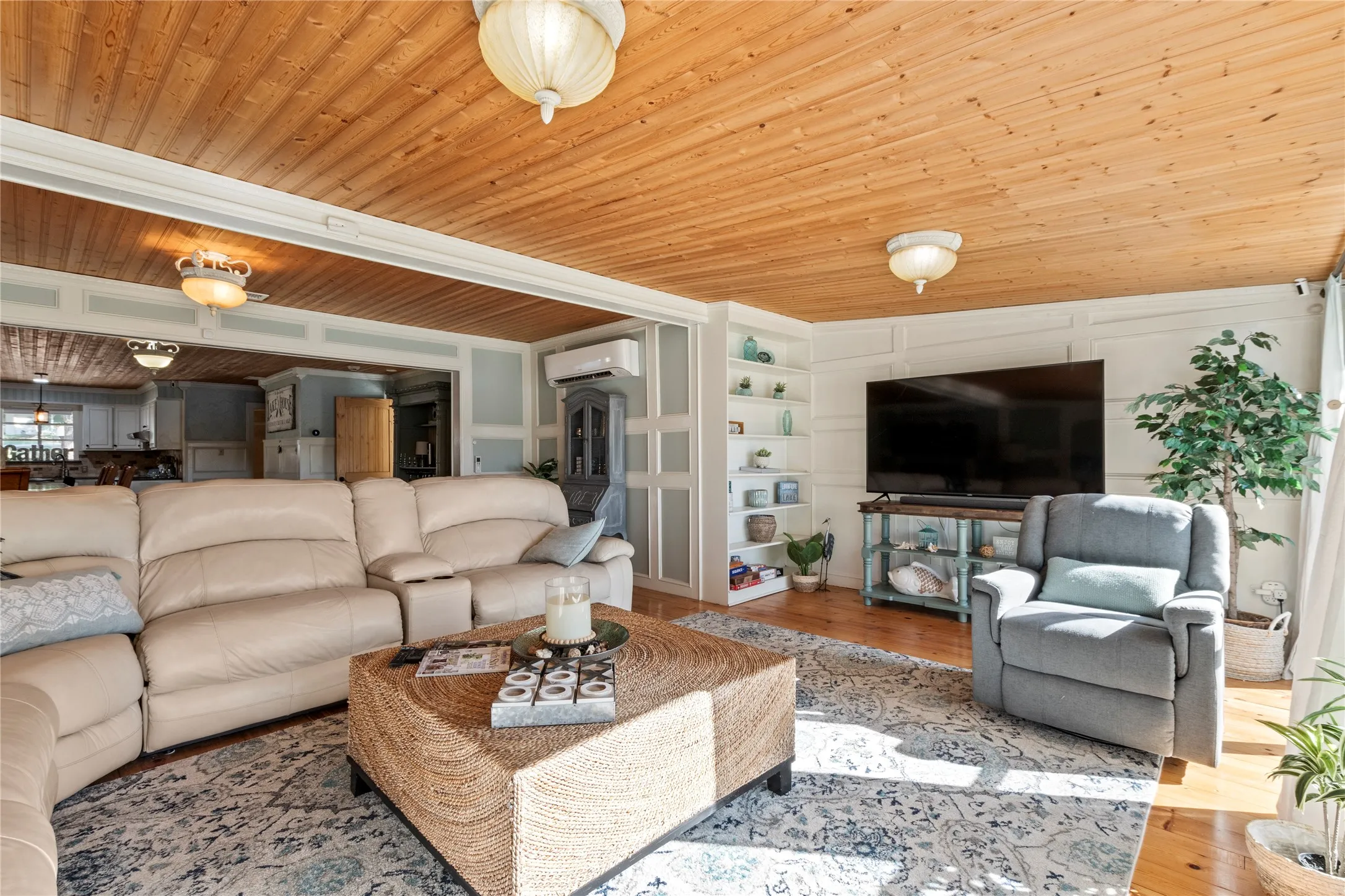 Natural wood-plank ceiling, wall paneling, built-in shelving, wall-mounted air conditioning unit, and wood-finish flooring