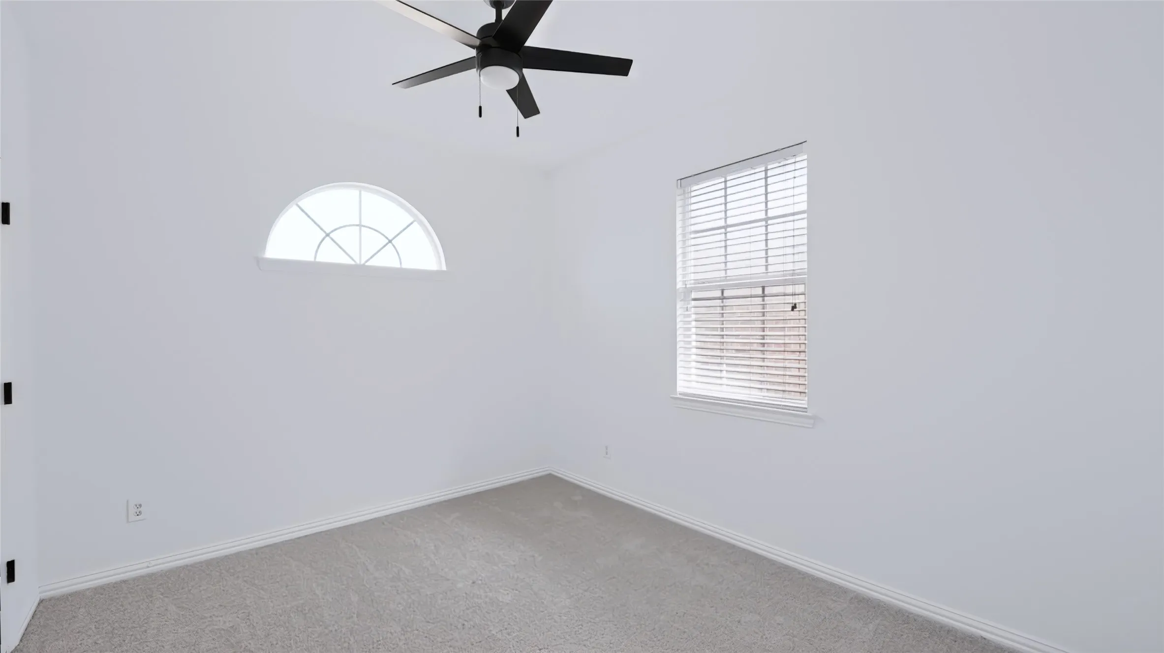 Room featuring neutral carpeting, arched window, standard single-hung window with installed blinds, and ceiling fan with integrated light fixture