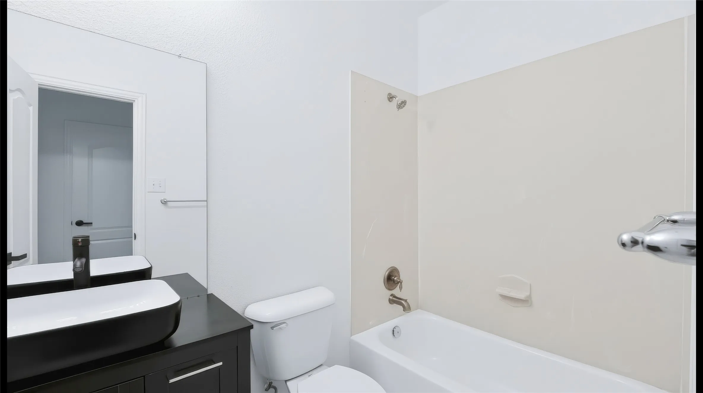 Bathroom featuring a dark wood-finish vanity, rectangular vessel sink, matte black faucet, and a combination tub and shower with light-toned wall surround