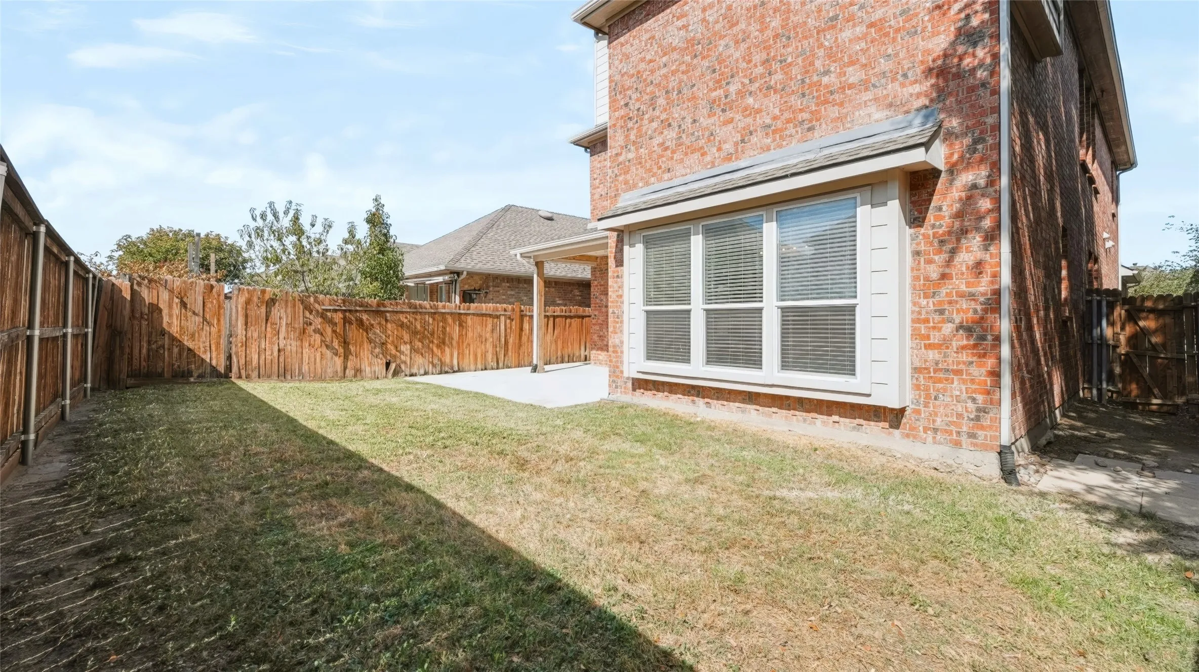 Rear exterior featuring red brick masonry, a concrete patio, and a wood privacy fence