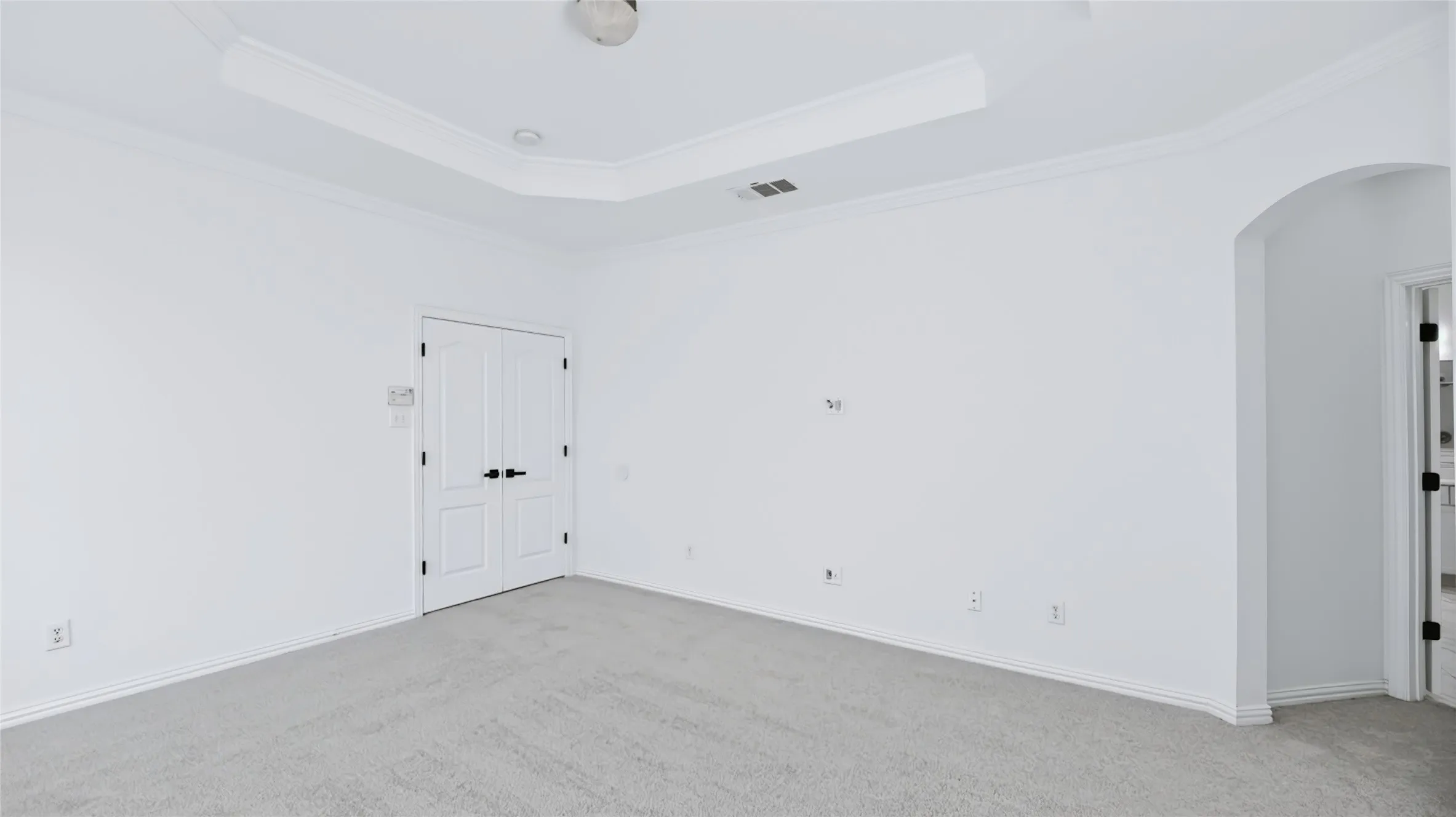 Room featuring a tray ceiling, neutral carpeting, double doors with matte black hardware, and an arched entry