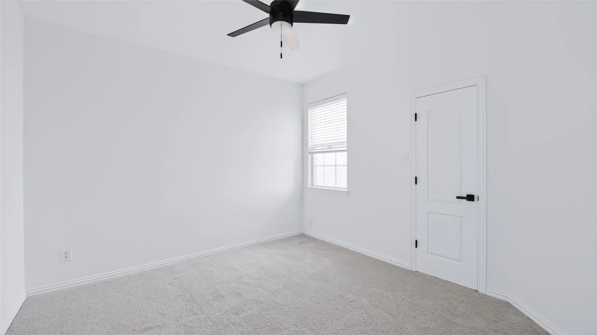 Neutral-toned carpeting, matte black ceiling fan, white interior door with matte black hardware, and window with built-in blinds