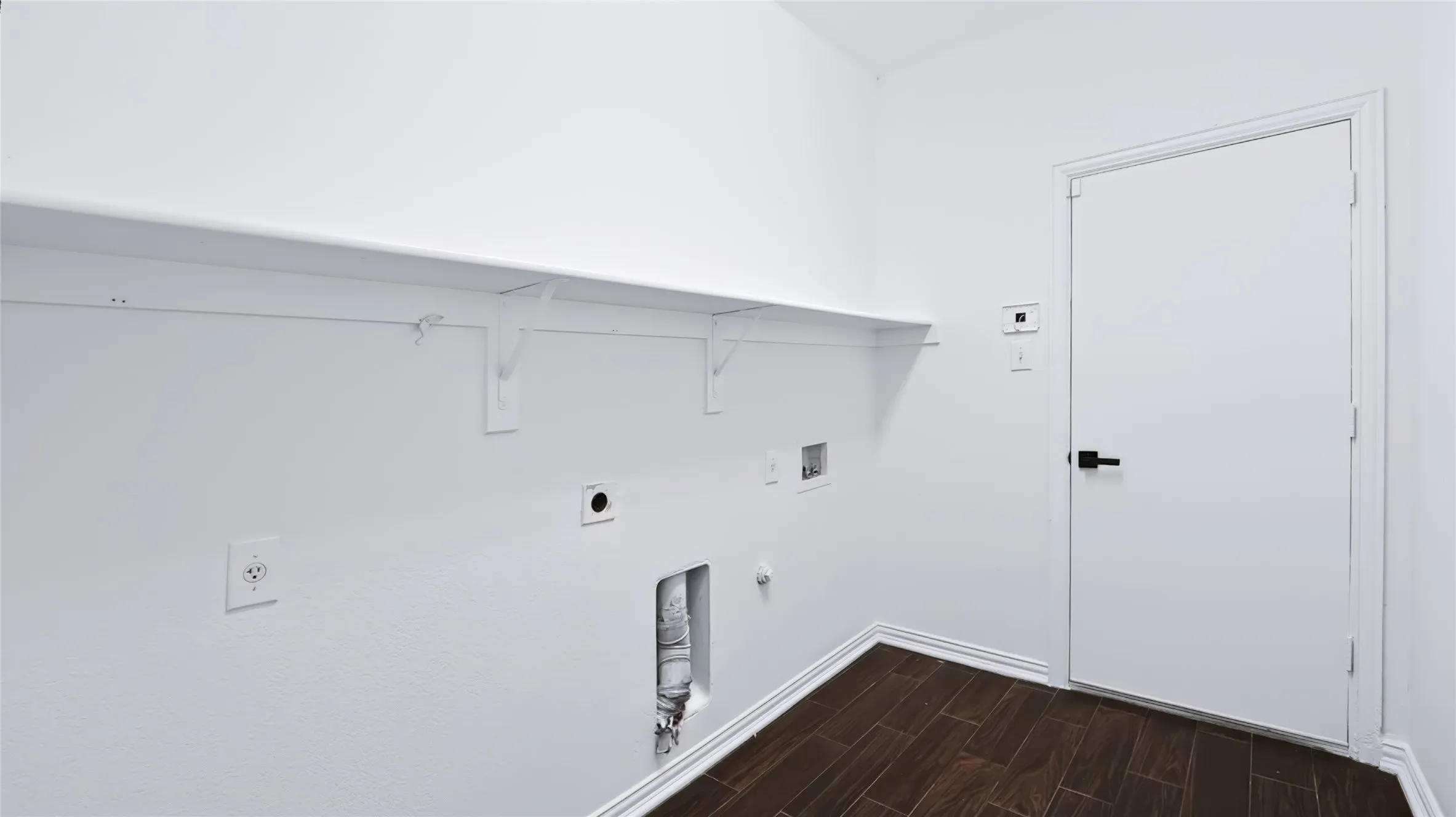 Utility area featuring wood-finish tile flooring, a full-length wall-mounted shelf, and a white interior door with matte black hardware