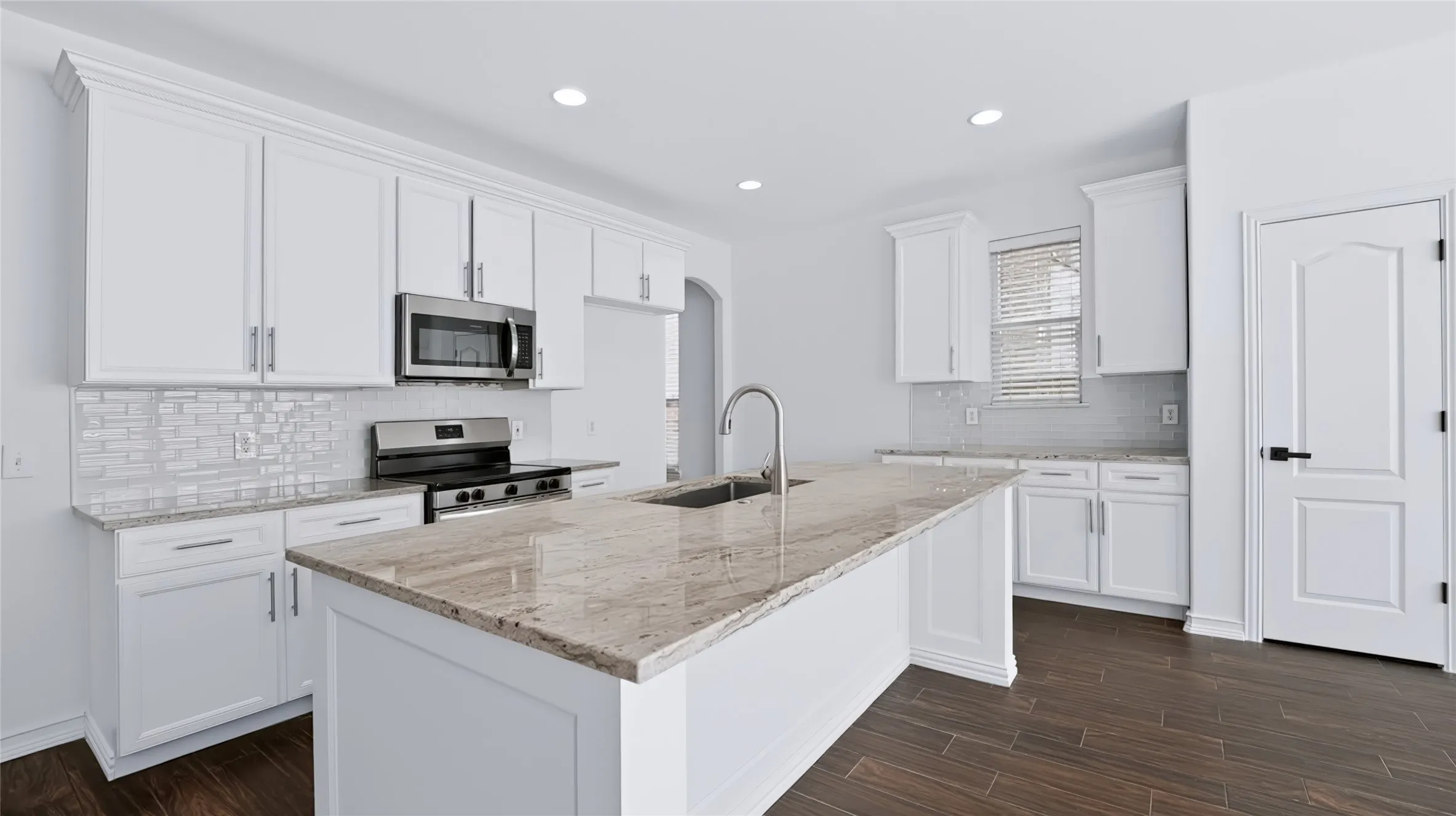 Kitchen featuring white cabinetry, stone countertops, central island, subway tile backsplash, and wood-finish tile flooring