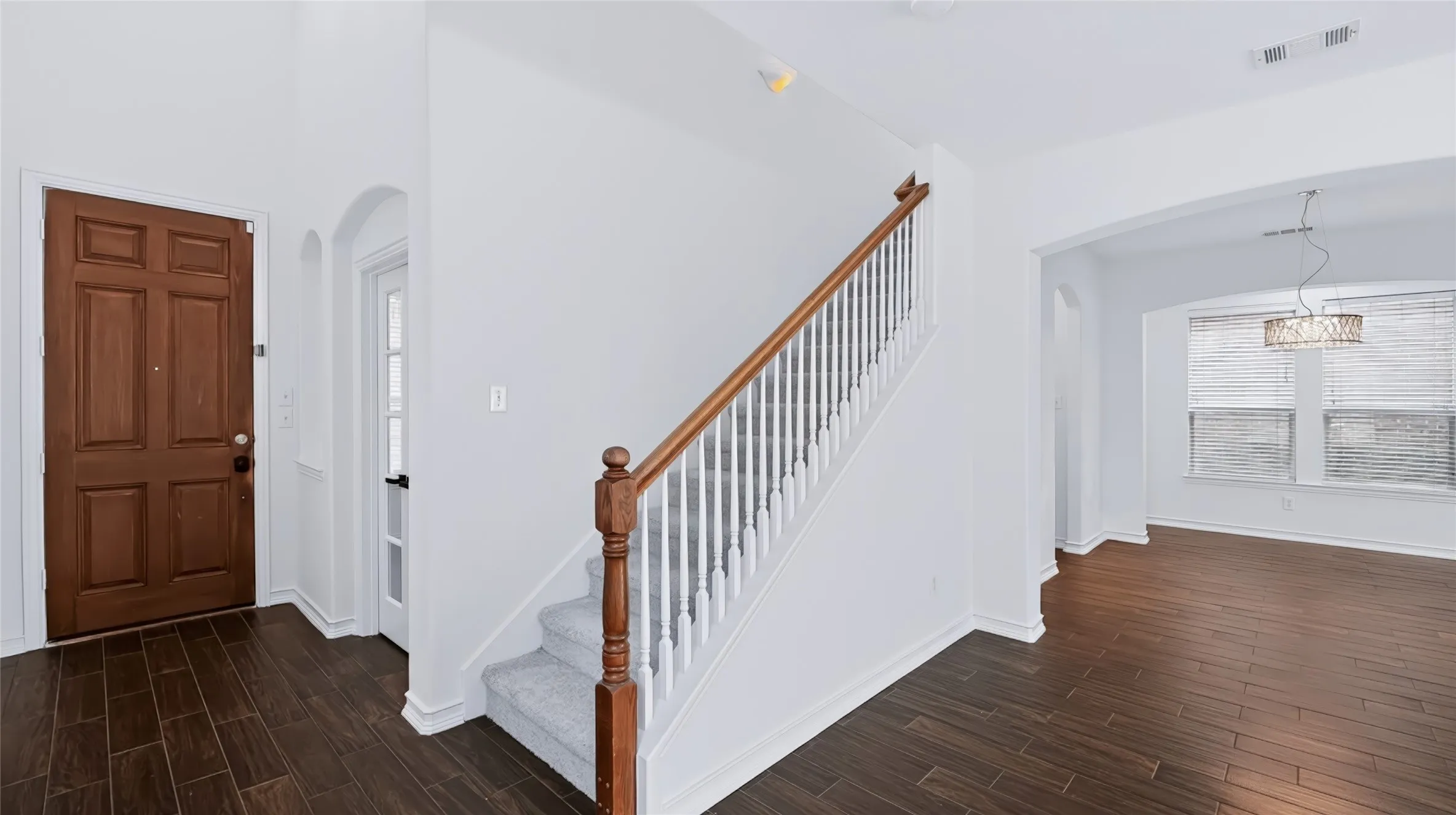Foyer featuring wood-finish tile flooring, staircase with white balusters and wood handrail, and arched architectural detailing