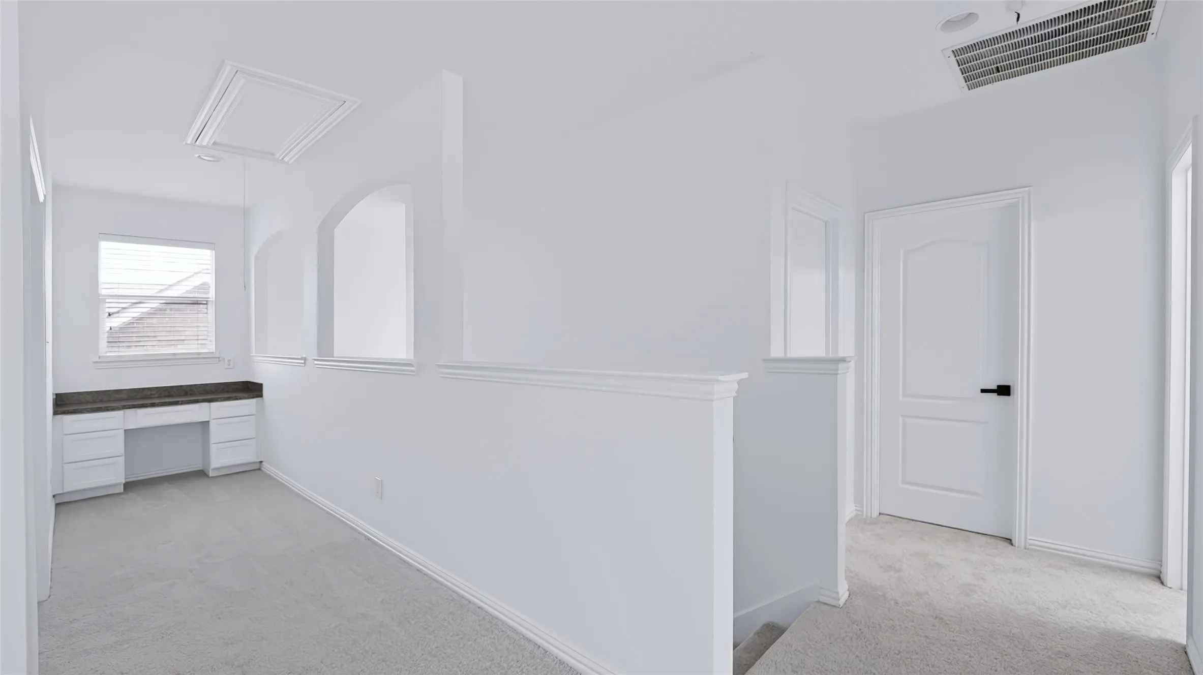 Built-in desk area with stone-finish countertop and cabinetry, arched architectural cutouts, wall-to-wall carpeting, and a multi-panel door with matte black hardware