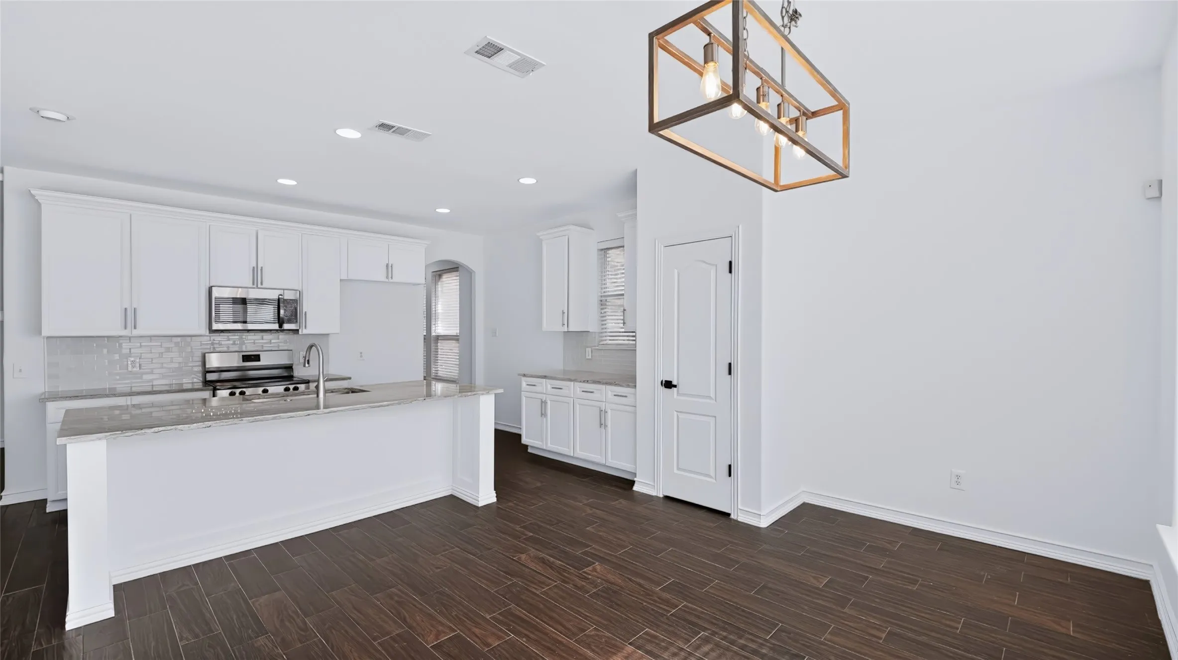 Kitchen featuring white shaker-style cabinetry, a stone-surfaced island with an integrated stainless steel sink, wood-finish tile flooring, recessed lighting, and a geometric metal-frame chandelier