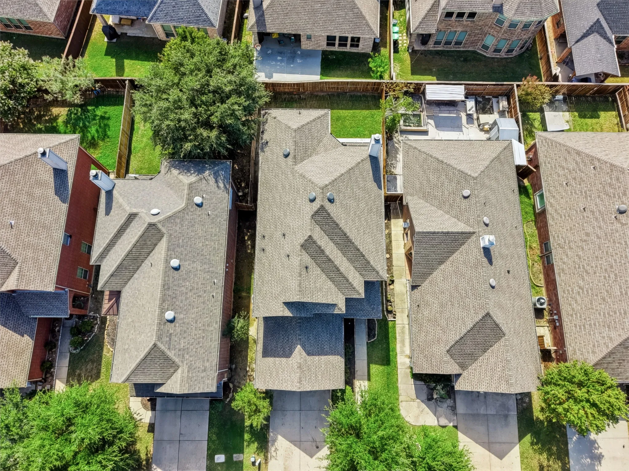Aerial perspective of residential property featuring a composition shingle roof, concrete driveway, and fenced backyard with grass lawn