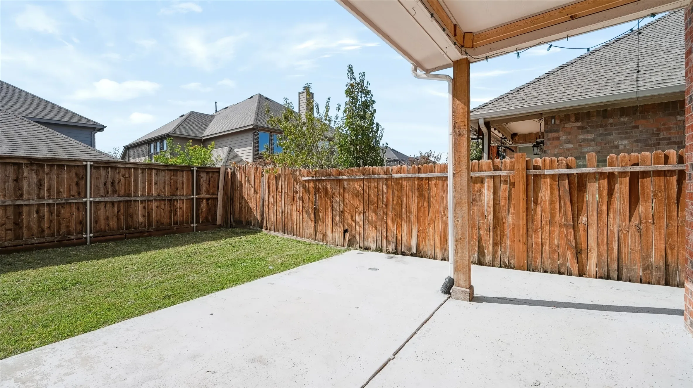Covered concrete patio featuring a wood support post, enclosed by a full-height wood privacy fence and a manicured lawn