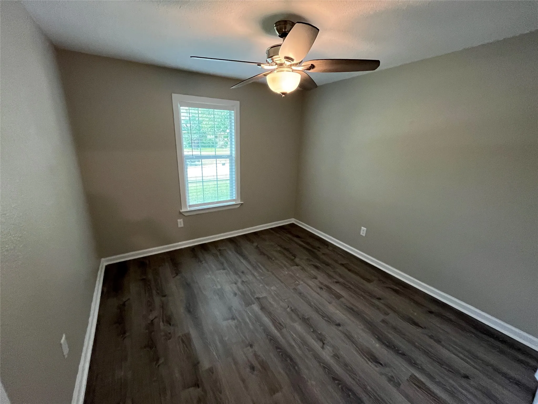 Room featuring wood-finish flooring, neutral wall paint, and a ceiling fan with integrated lighting, centered by a single window with blinds