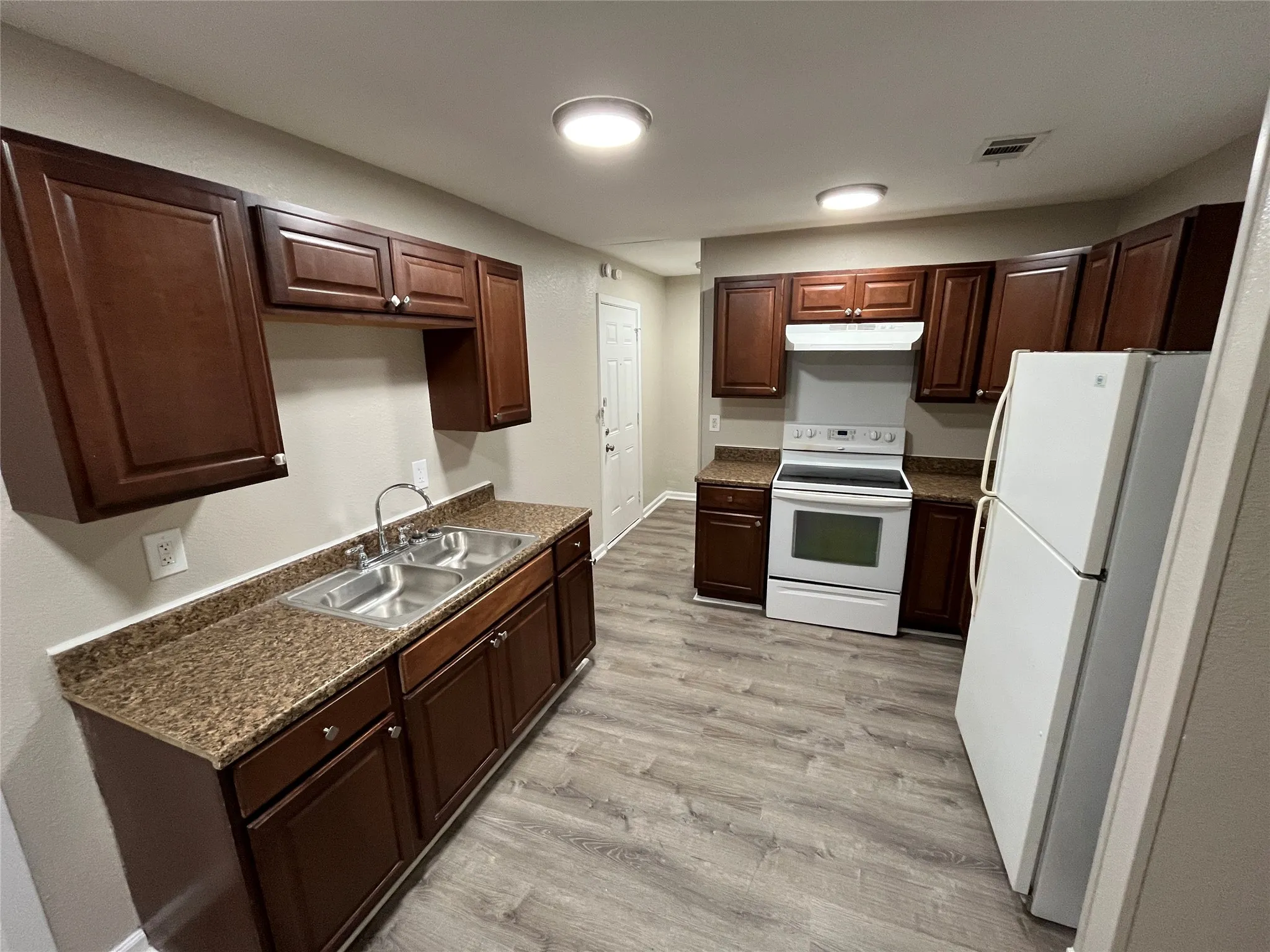 Kitchen featuring dark wood-finish cabinetry, stone-finish laminate countertops, dual-basin stainless steel sink, and wood-finish flooring