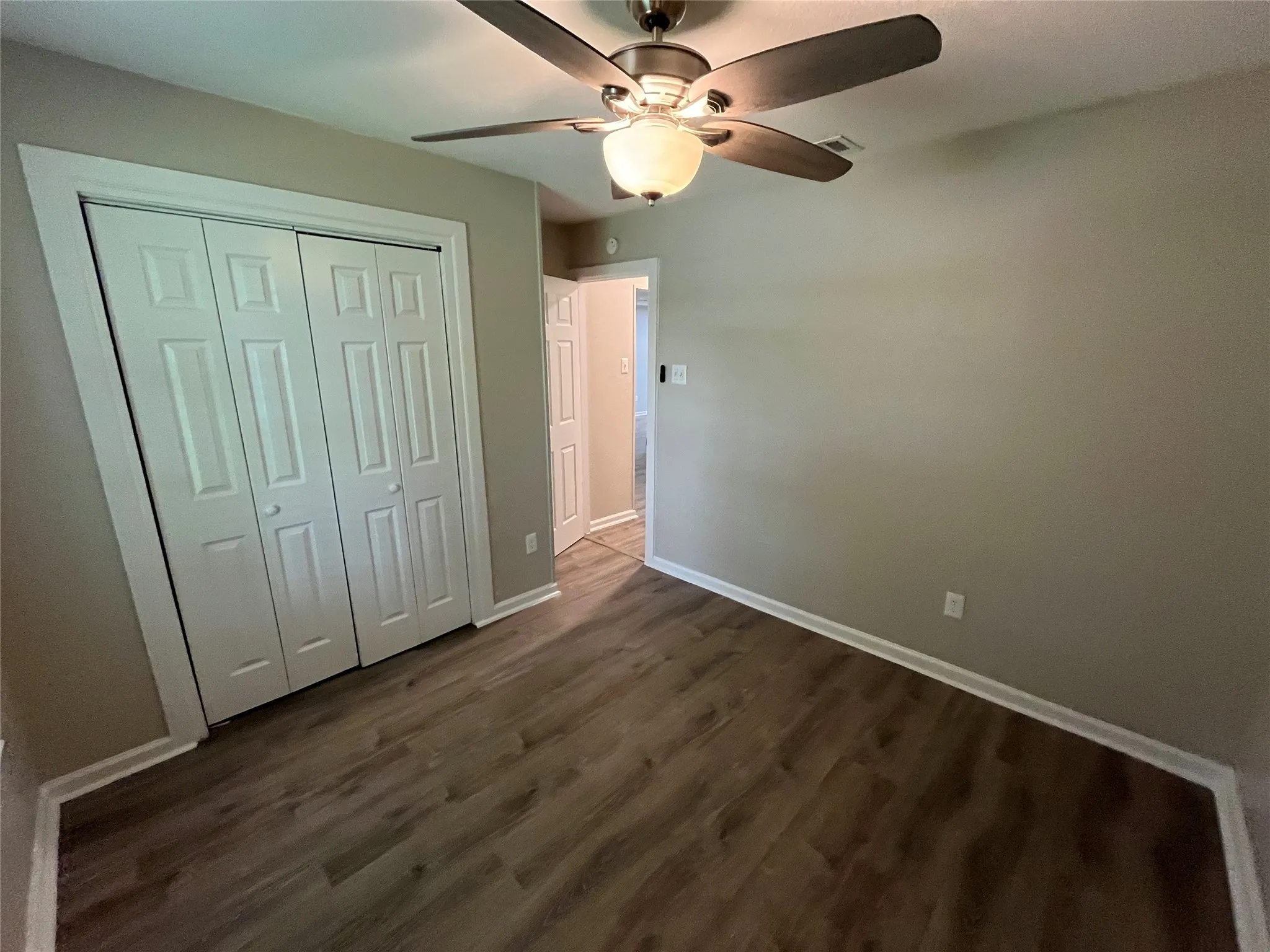Neutral-toned room featuring wood-finish flooring, a multi-panel bi-fold closet, and a ceiling fan with integrated lighting