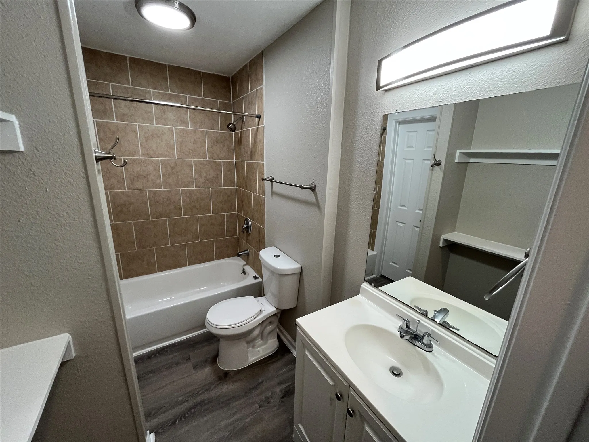 Bathroom featuring wood-finish flooring, vanity with integrated sink, rectangular mirror with integrated lighting, and tile-surround shower and tub combination