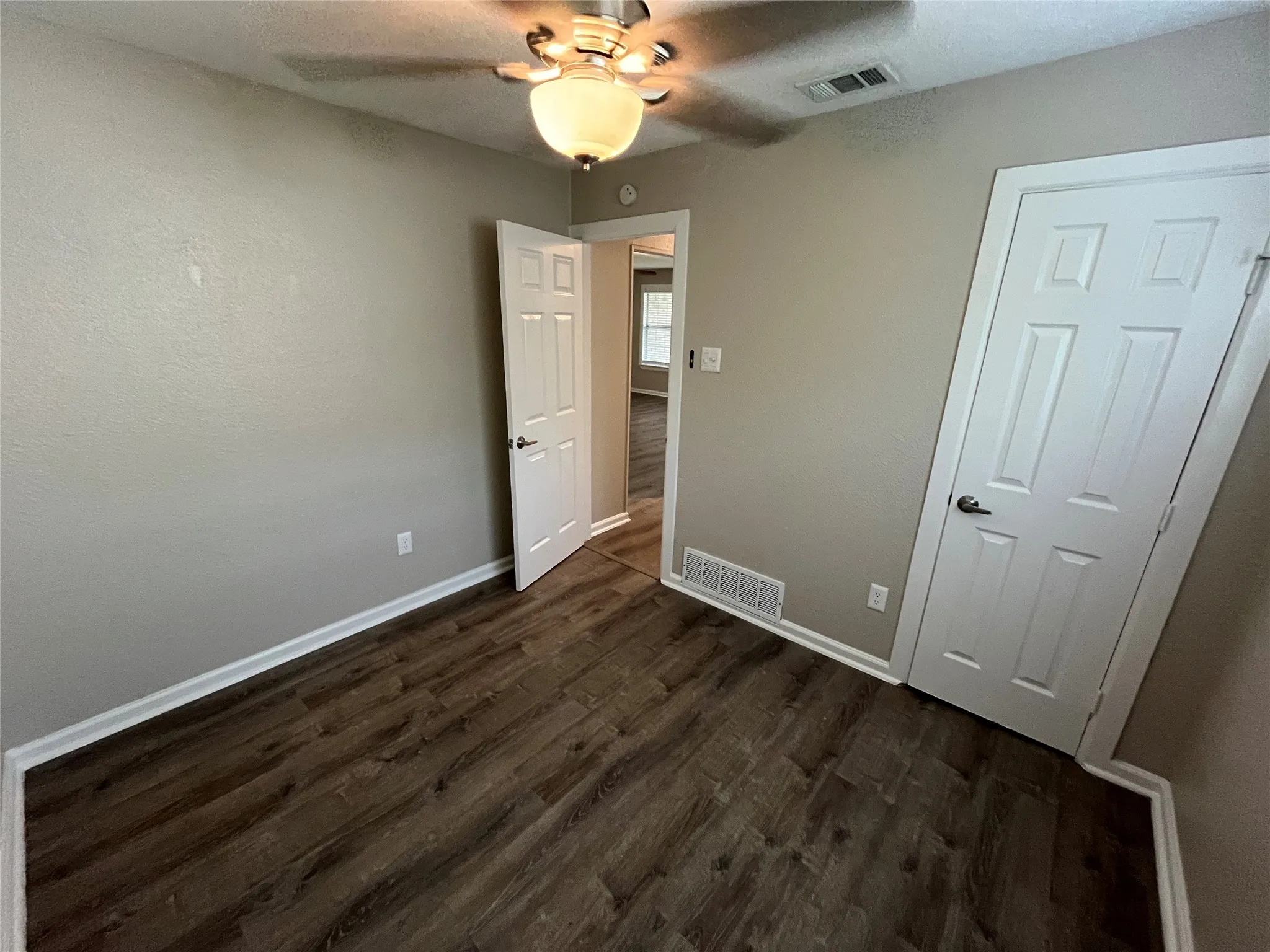 Room featuring wood-finish flooring, six-panel interior doors, and a ceiling-mounted light fixture with a fan