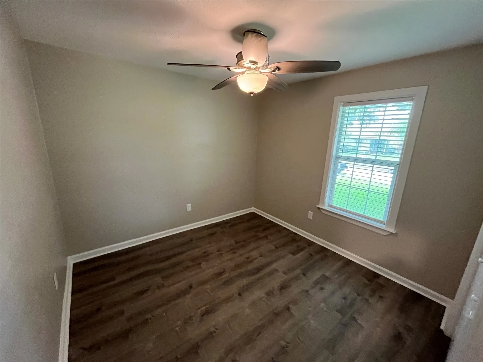 Wood-finish flooring, multi-pane window with horizontal blinds, and a multi-blade ceiling fan featuring integrated dual light fixtures