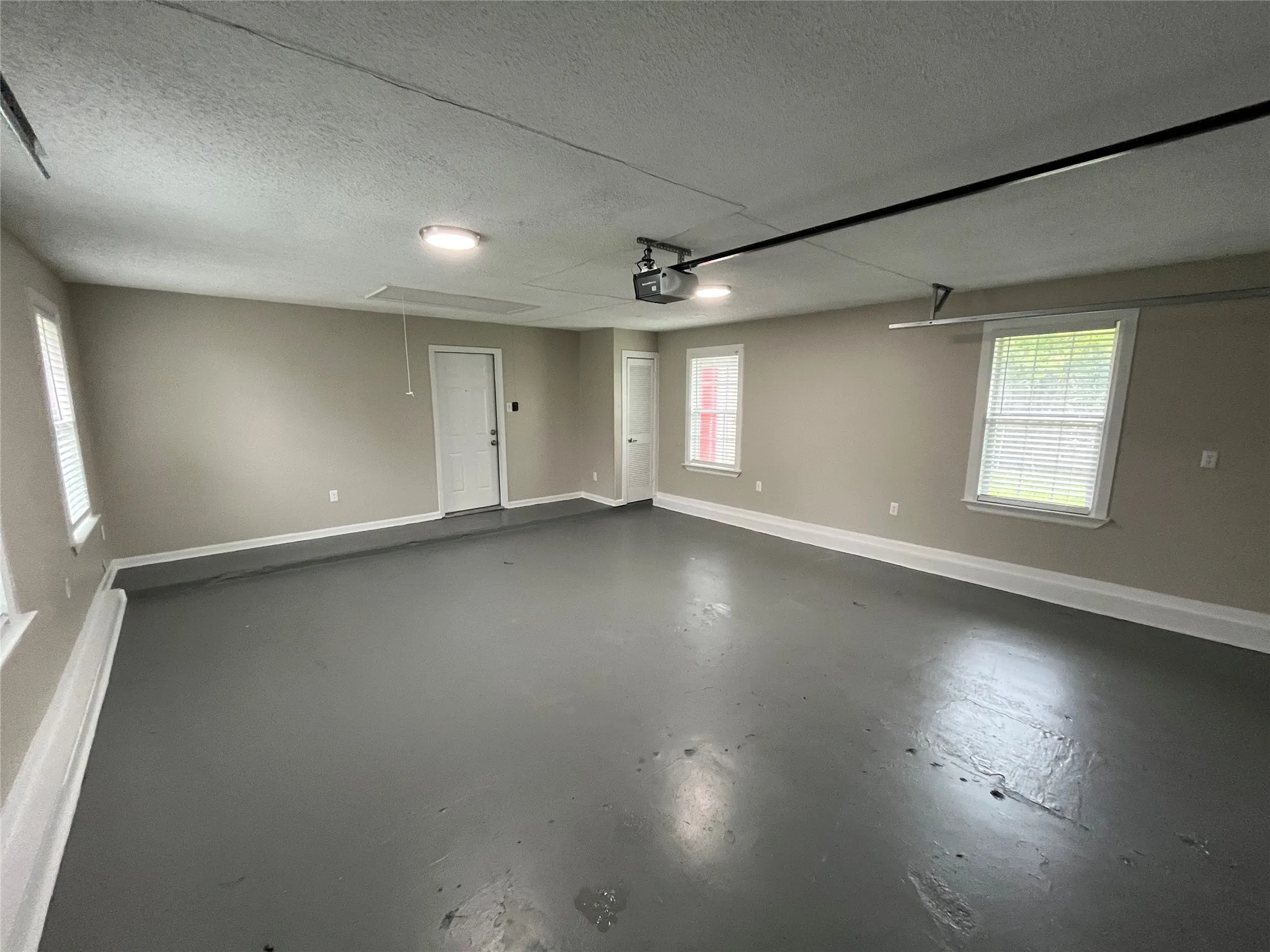 Finished interior space featuring painted concrete flooring, neutral wall tones, three multi-pane windows, and an overhead garage door opener