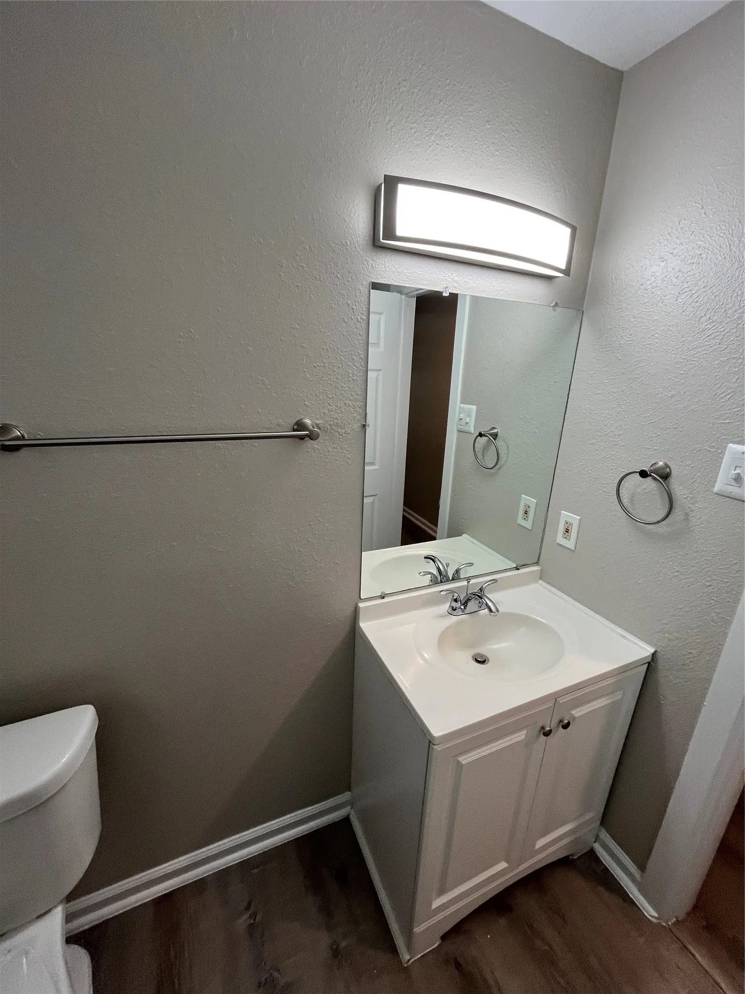 Vanity cabinet with white shaker-style doors, integrated sink, polished metal faucet, rectangular wall-mounted light fixture, and large flat mirror
