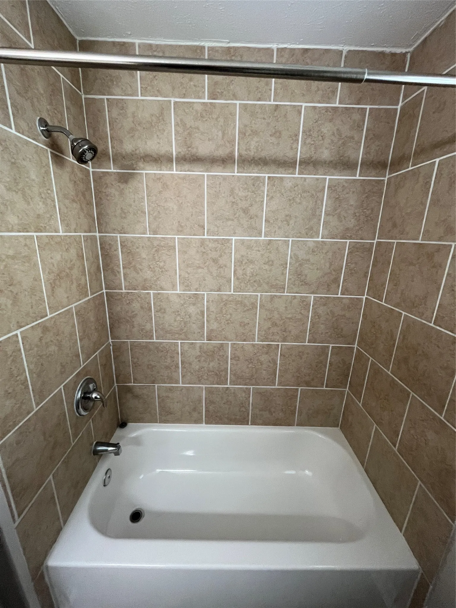 Bathtub featuring a white acrylic finish, full-height tile surround, chrome faucet hardware, and a mounted showerhead