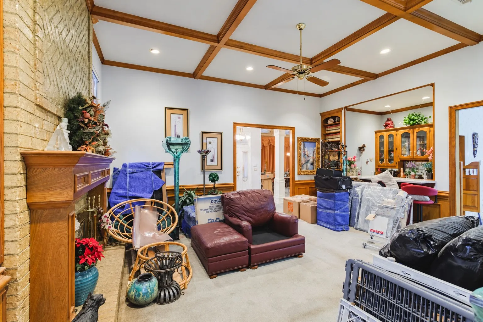 Living area featuring a coffered wood ceiling, brick fireplace with a wood mantel, built-in wooden shelving, and recessed lighting