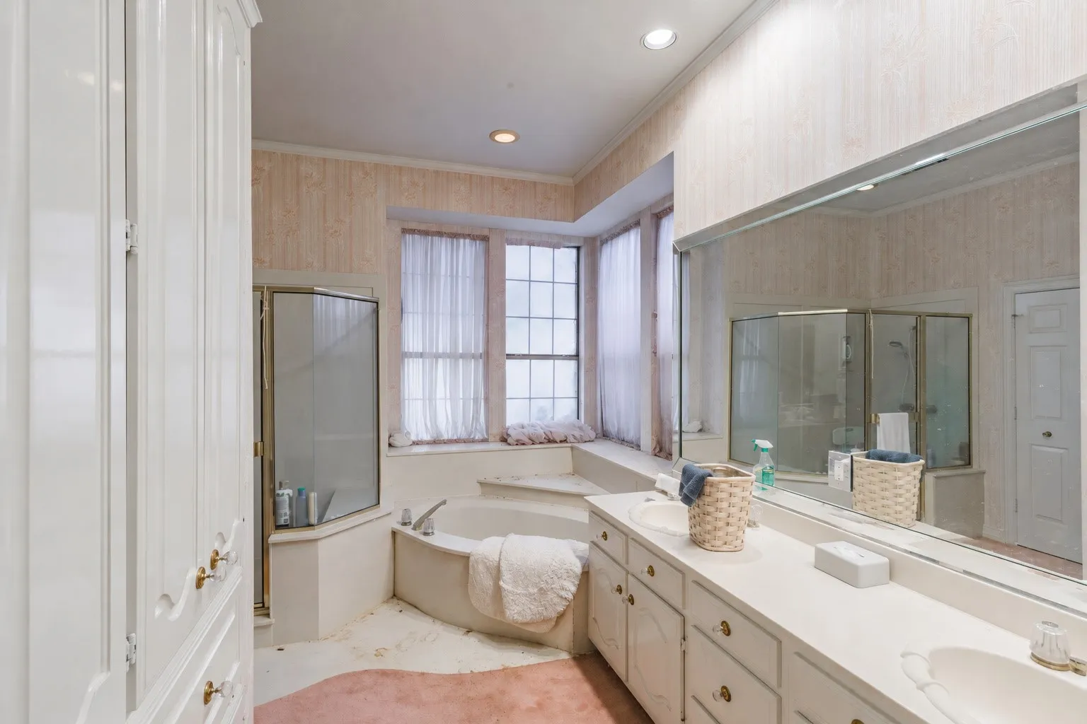 Bathroom featuring a dual-sink vanity with white cabinetry, a large wall-mounted mirror, a jetted soaking tub, a glass-enclosed shower, and recessed ceiling lighting