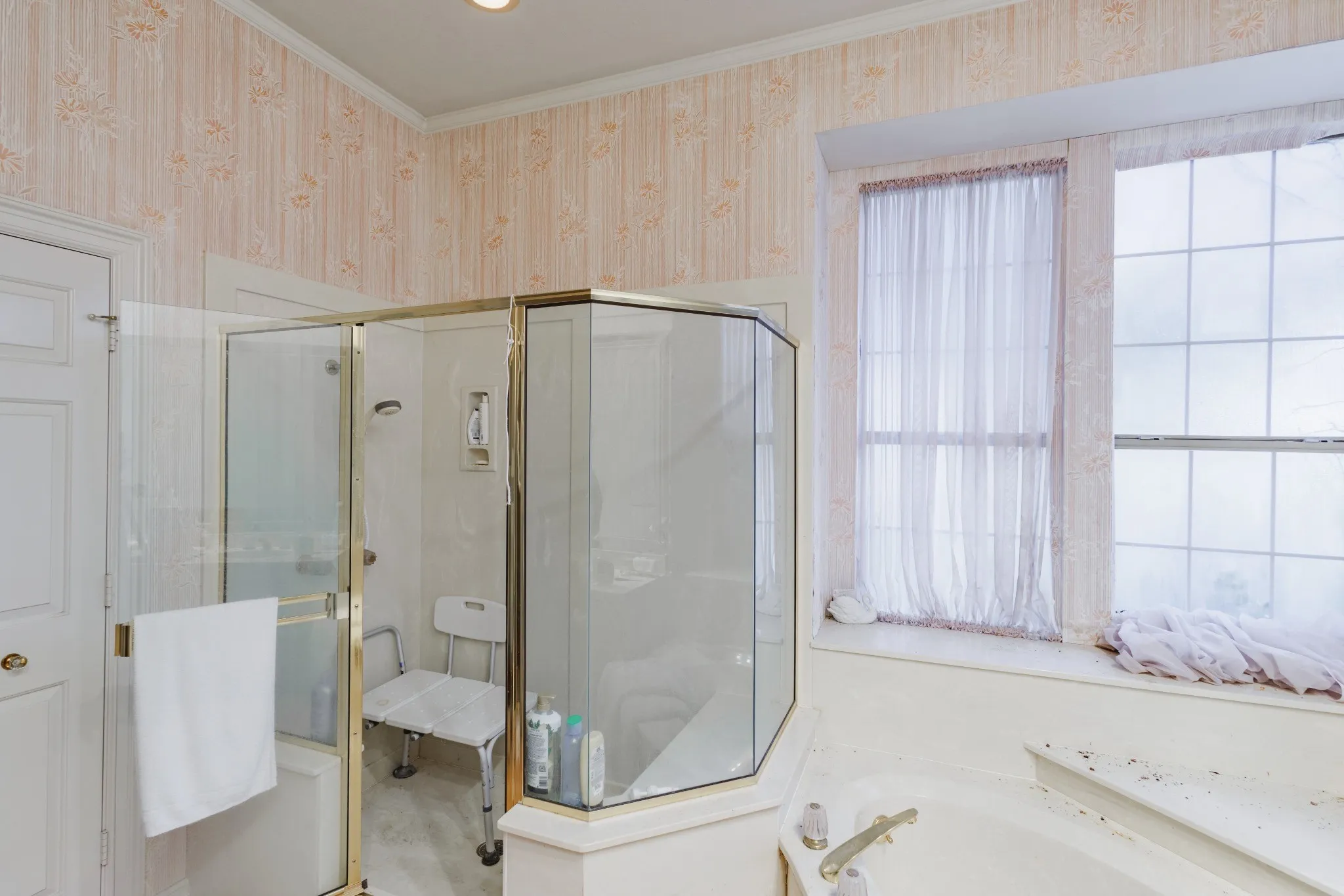 Corner shower enclosure with gold-tone hardware, built-in soaking tub, and expansive multi-pane window with interior ledge