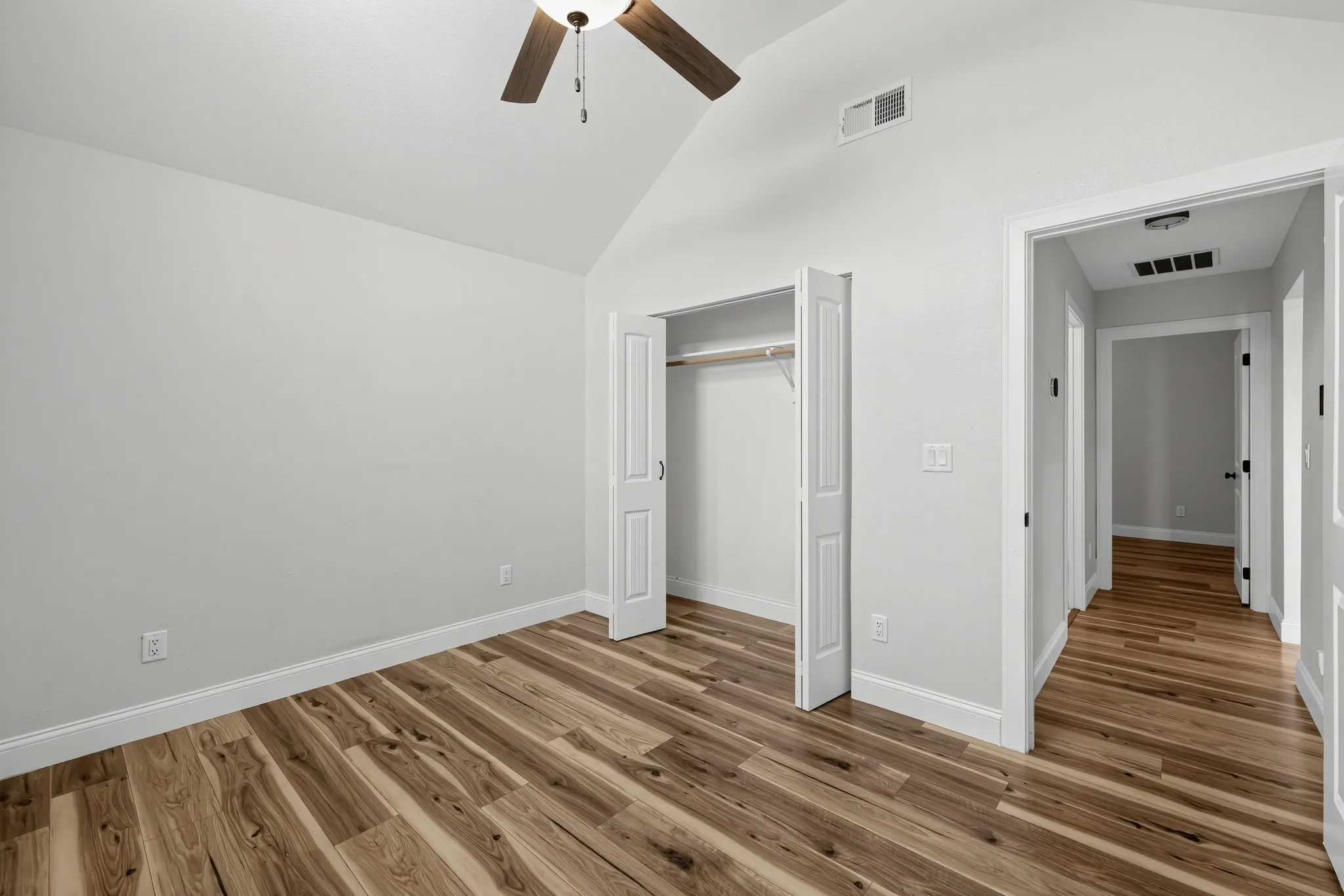 Vaulted ceiling with integrated ceiling fan, wood-finish flooring, and closet with bifold doors