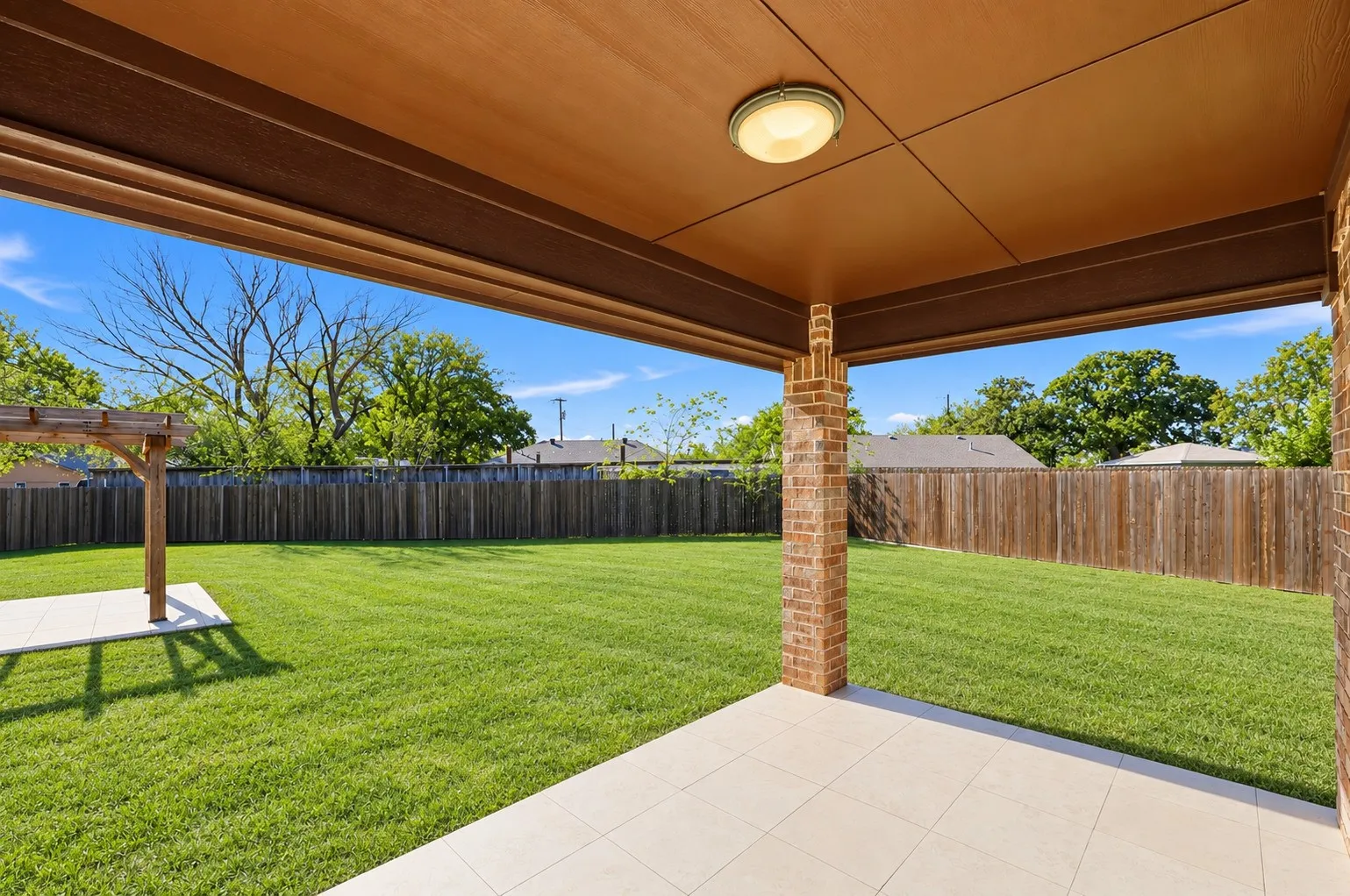 Covered patio with a tile floor and flush-mount lighting, brick structural column, and a wood pergola