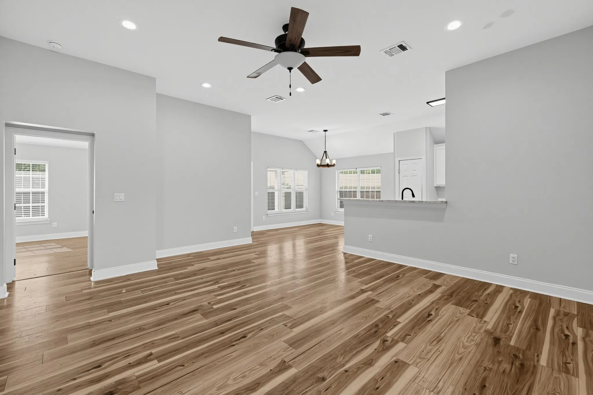 Open floor plan featuring wood-finish flooring, vaulted ceilings, recessed lighting, a ceiling fan with integrated lighting, and a kitchen breakfast bar with stone-finish countertops
