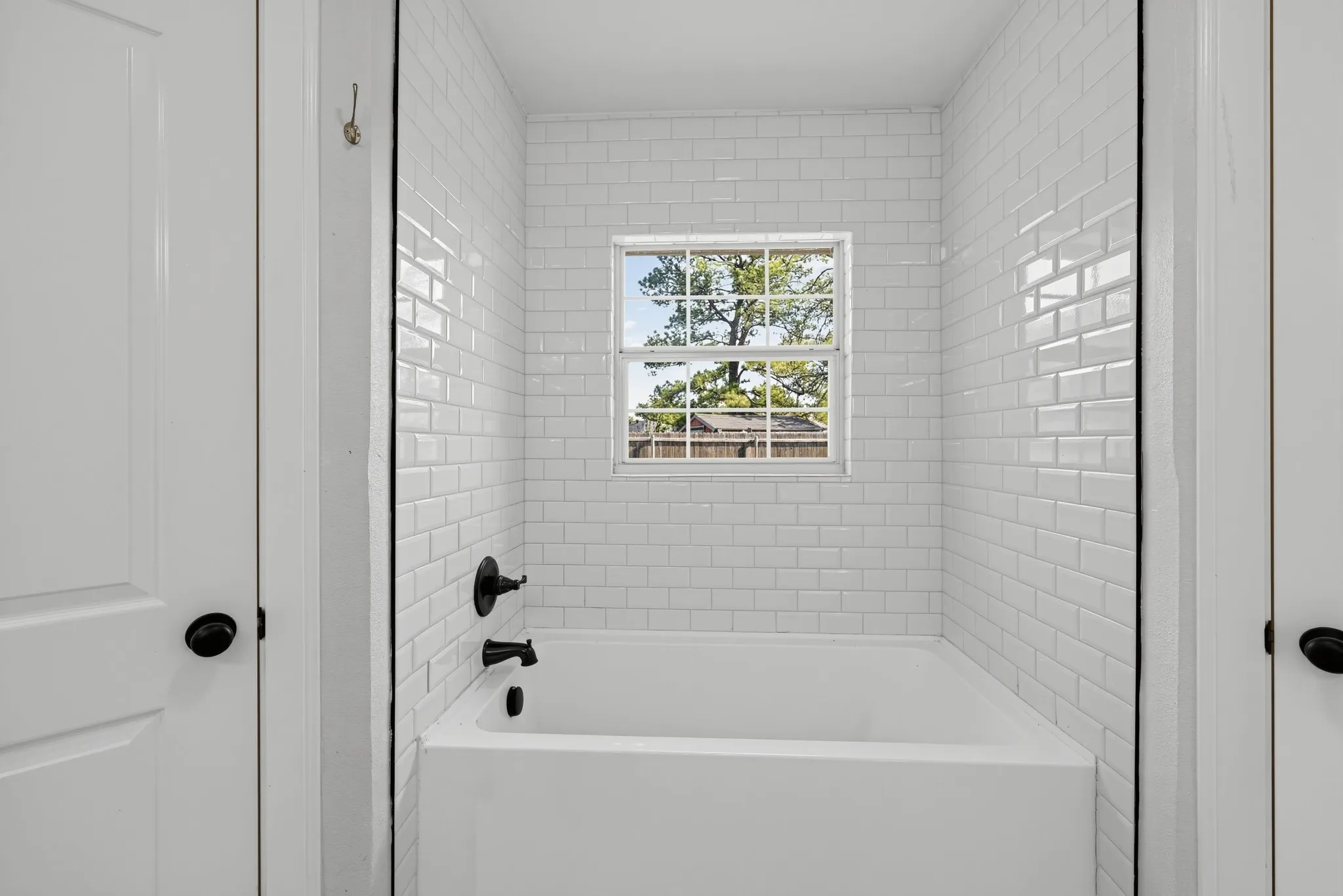 Bathtub alcove featuring white subway tile surround, matte black plumbing fixtures, and a single-hung window