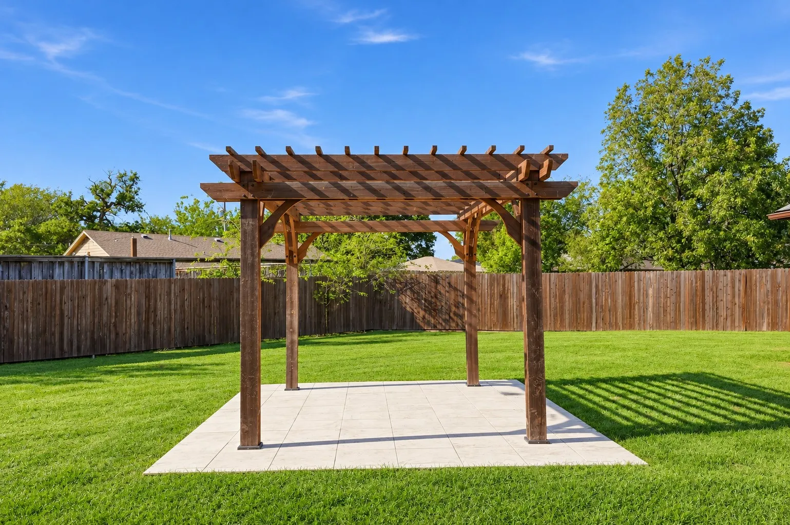 Backyard featuring a wood pergola, a square paved patio, and a manicured lawn enclosed by a wood privacy fence