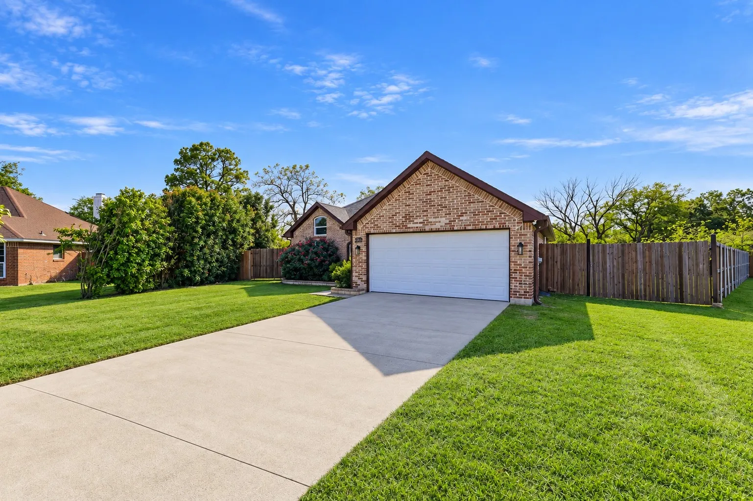Brick exterior featuring a front-facing attached two-car garage, concrete driveway, and wooden privacy fencing
