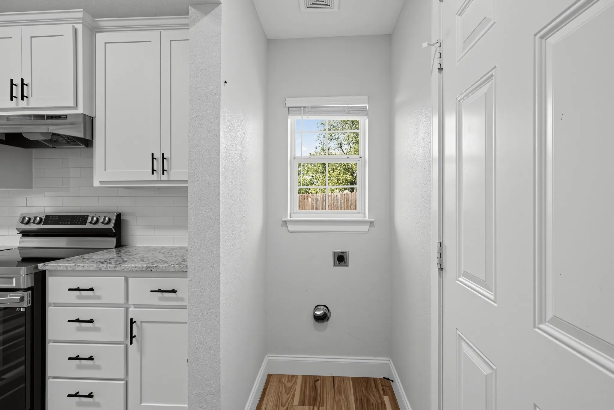 Utility area featuring wood-finish flooring, shaker-style cabinetry with matte black hardware, stone-finish countertops, subway tile backsplash, and a single-hung window