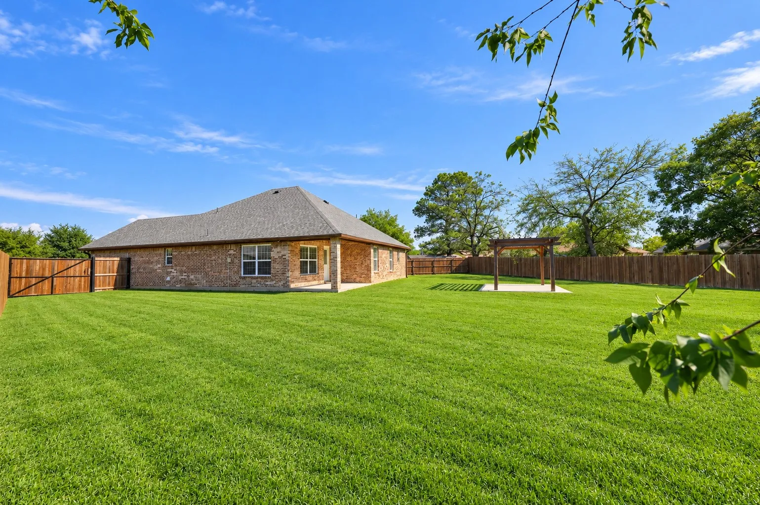 Brick exterior siding, rear covered patio, detached wooden pergola, and expansive fenced-in lawn