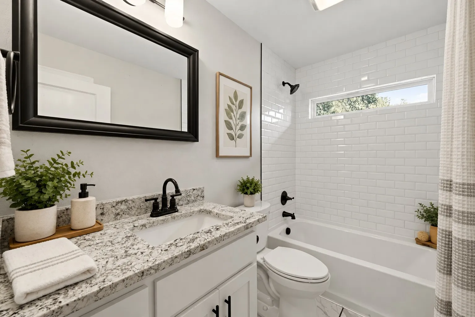 Bathroom featuring a stone-composite countertop, white subway tile shower surround, matte black hardware, horizontal transom window, and framed mirror