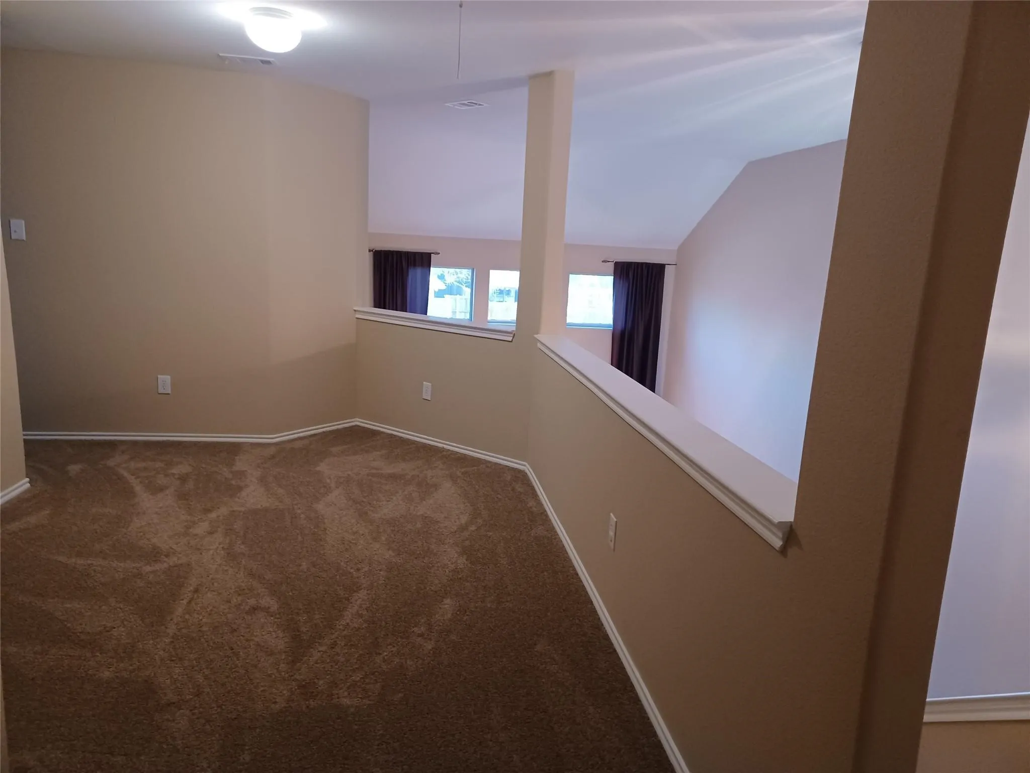 Carpeted loft area with a partial wall overlooking a lower space and vaulted ceilings