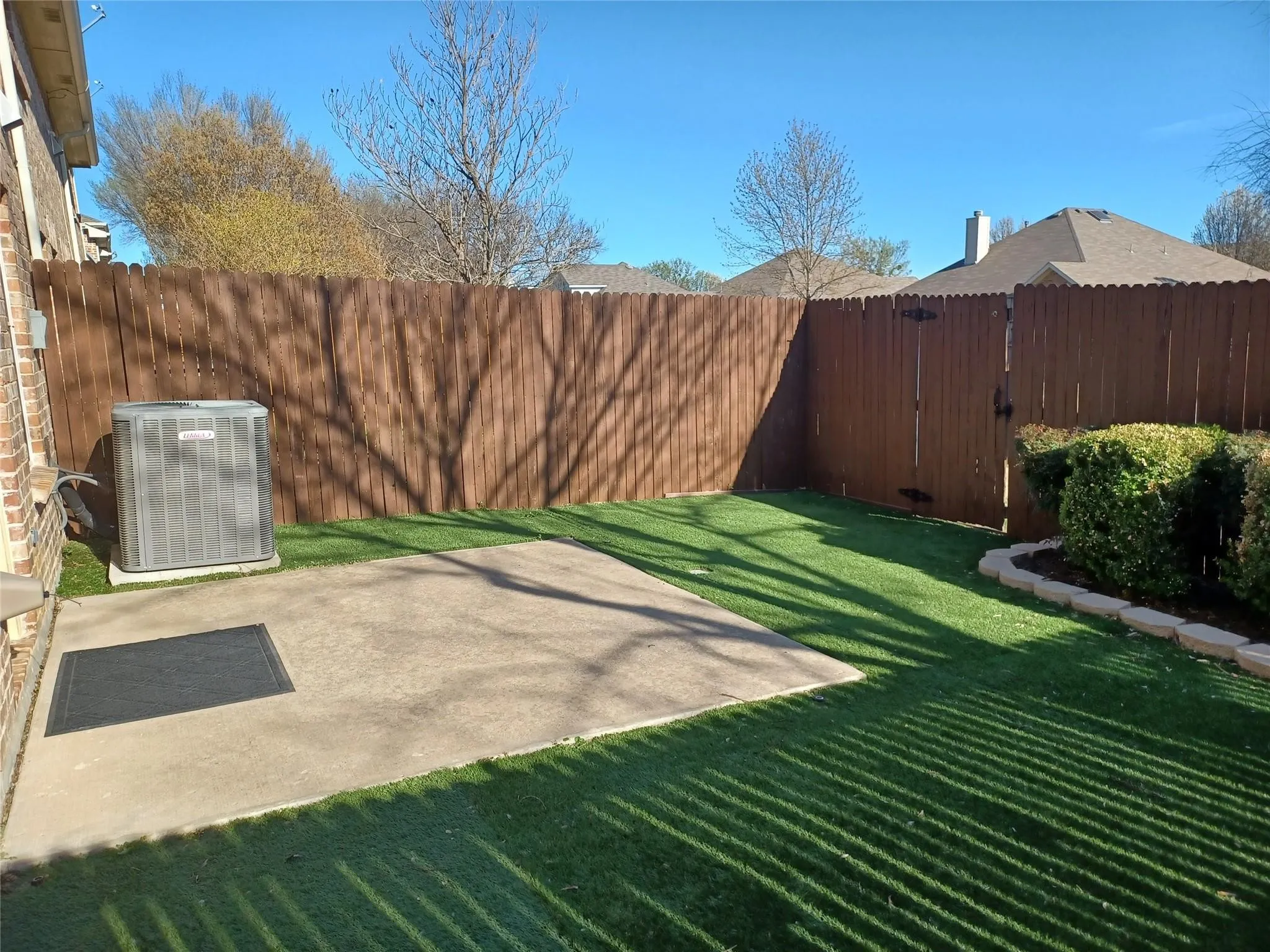 Private outdoor space featuring artificial turf, a concrete patio, and a wood privacy fence with gate access