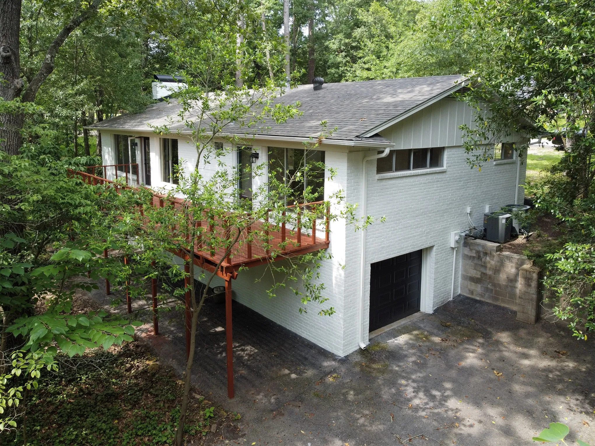 Painted brick exterior featuring an elevated wood deck, horizontal windows, and an attached lower-level garage
