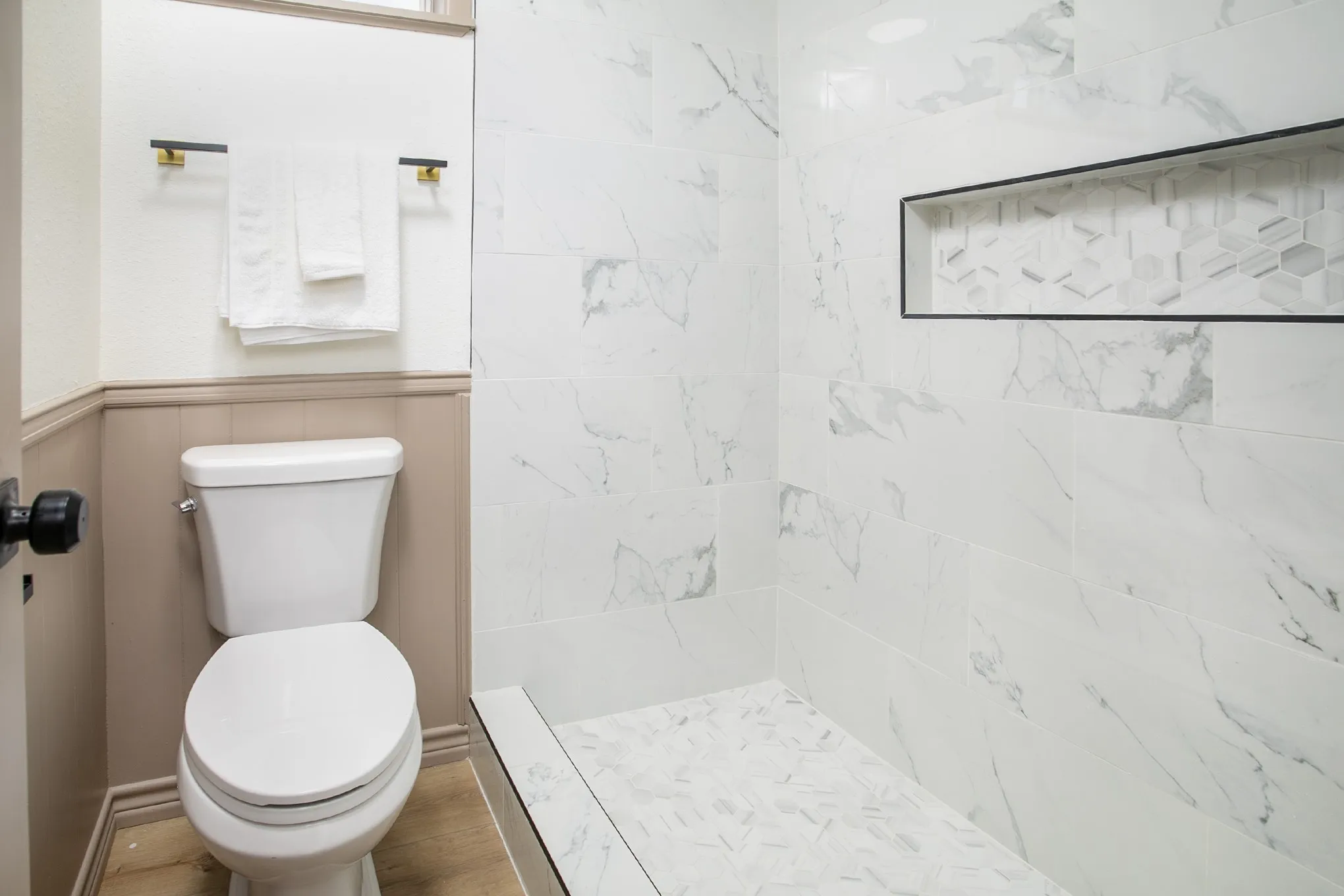 Walk-in shower featuring large-format stone-finish wall tile, a geometric-patterned inset storage niche, a mosaic-tiled floor, and wood-finish flooring