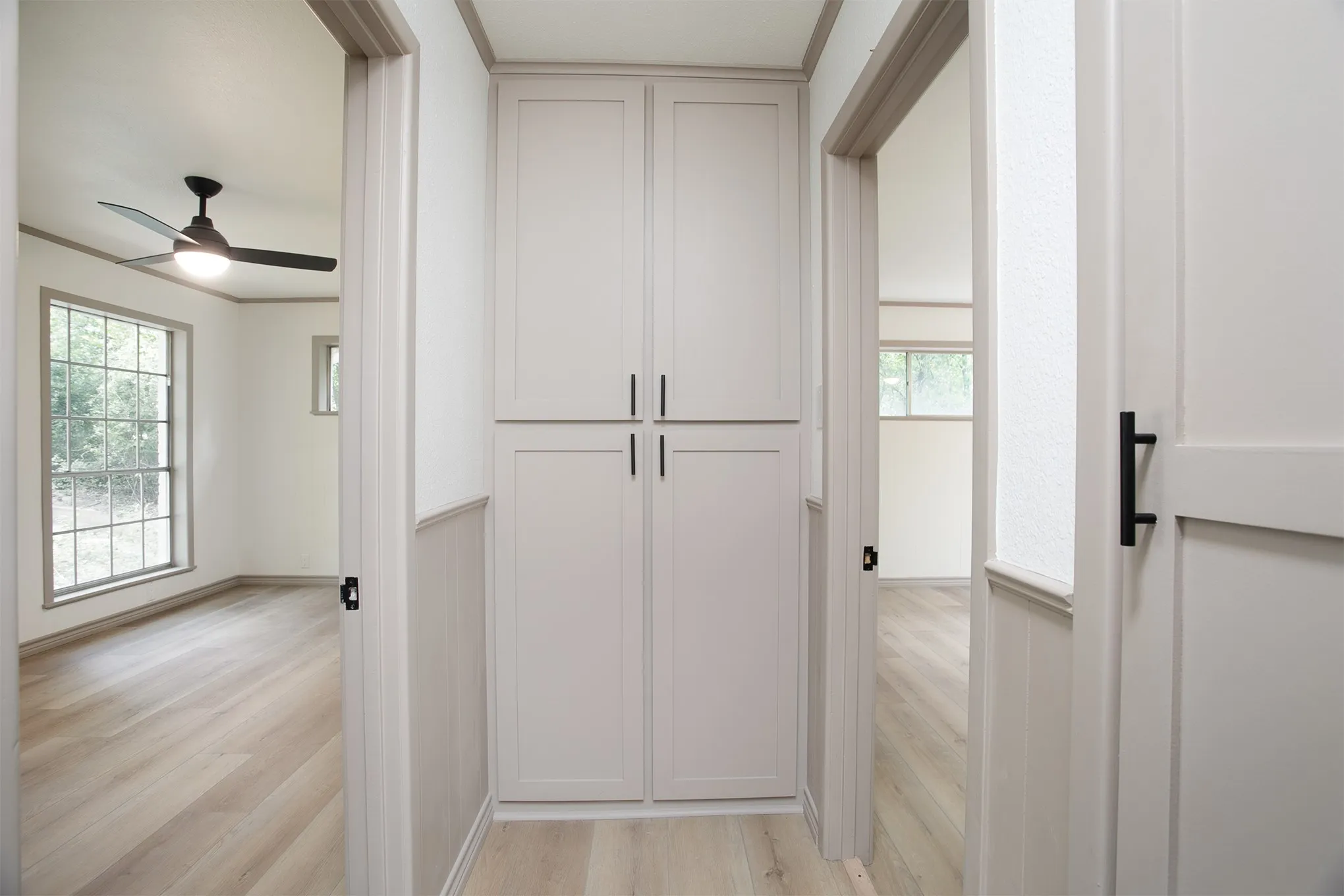 Hallway featuring floor-to-ceiling built-in cabinetry, wood-finish flooring, and shaker-style doors with matte black hardware