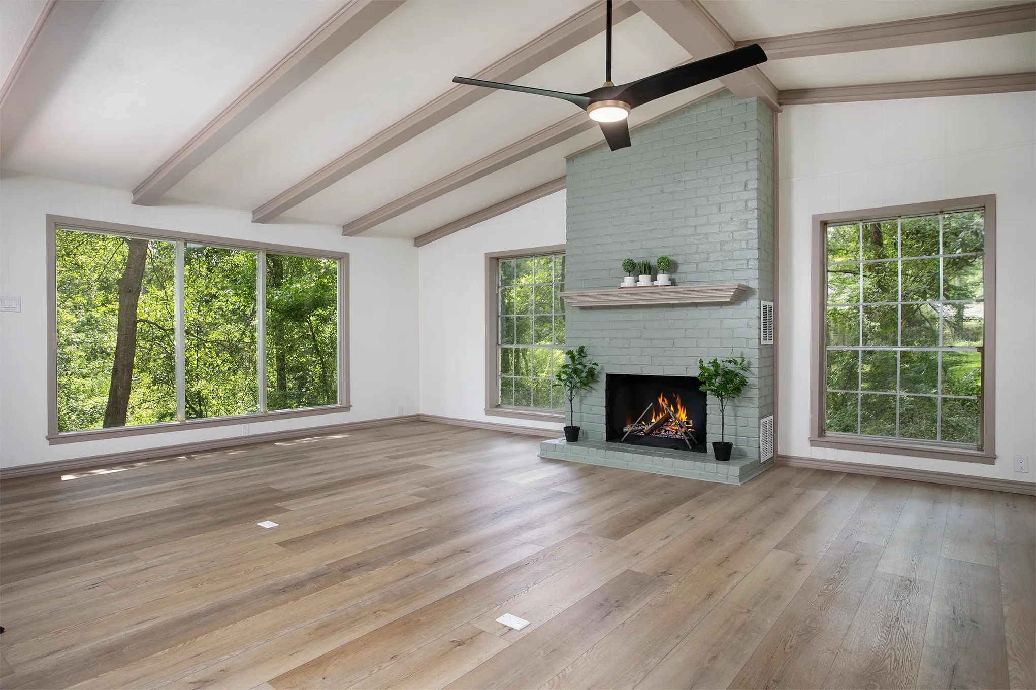 Vaulted ceilings with exposed beams, wood-finish flooring, painted brick fireplace with a mantel, and oversized windows