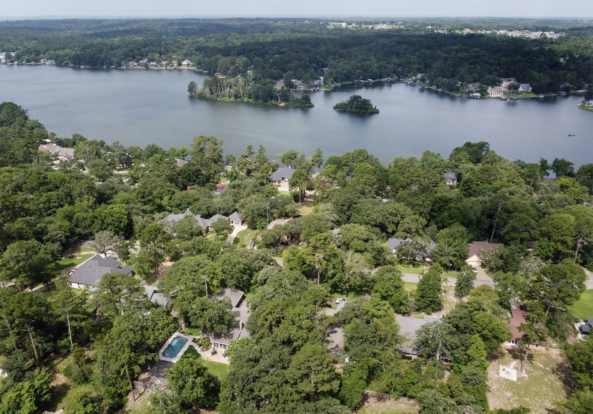 Aerial perspective featuring a residential lot with a private rectangular swimming pool, dense perimeter tree canopy, and direct proximity to a large inland lake